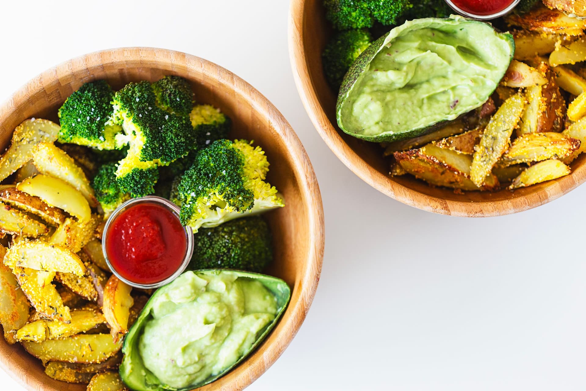 Taça com batatas assadas crocantes, brócolos a vapor, guacamole e ketchup.