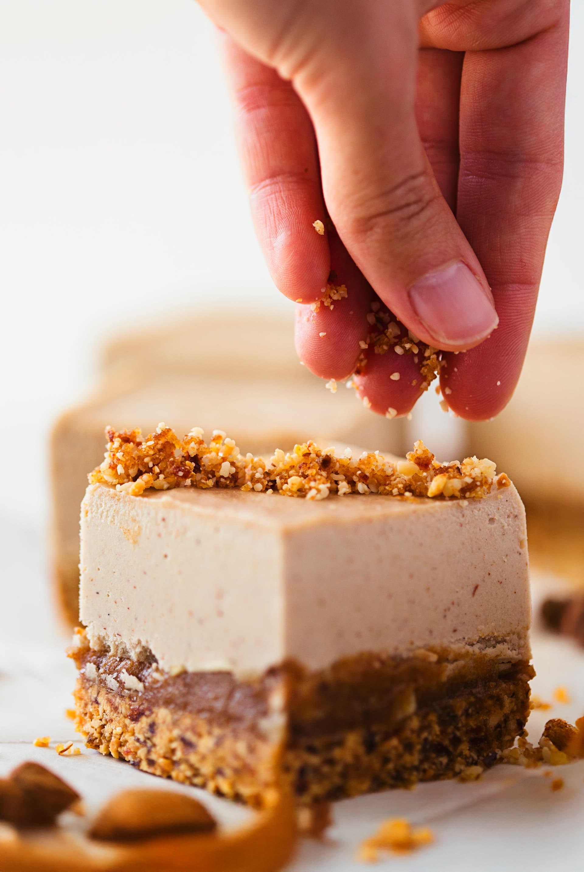 Mão a espalhar amêndoas picadas e crumble sobre o cheesecake.