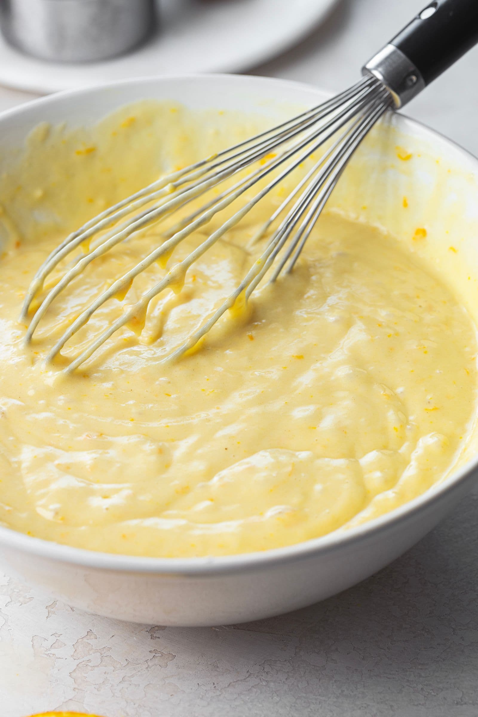 Creamy orange cake batter in a white bowl, ready to be poured into the pan.