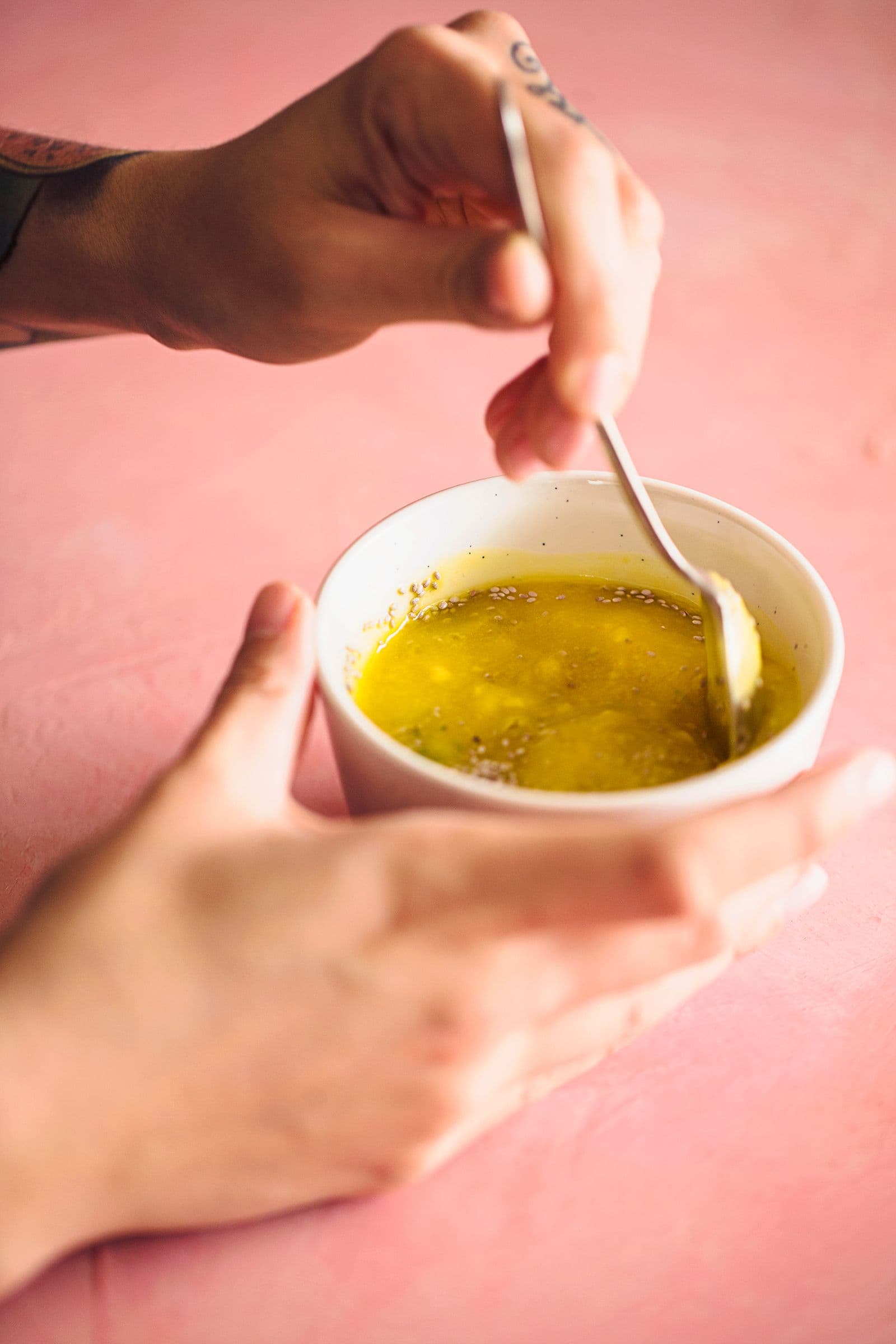 Mãos a mexer a mistura de manga e chia numa taça branca com uma colher.