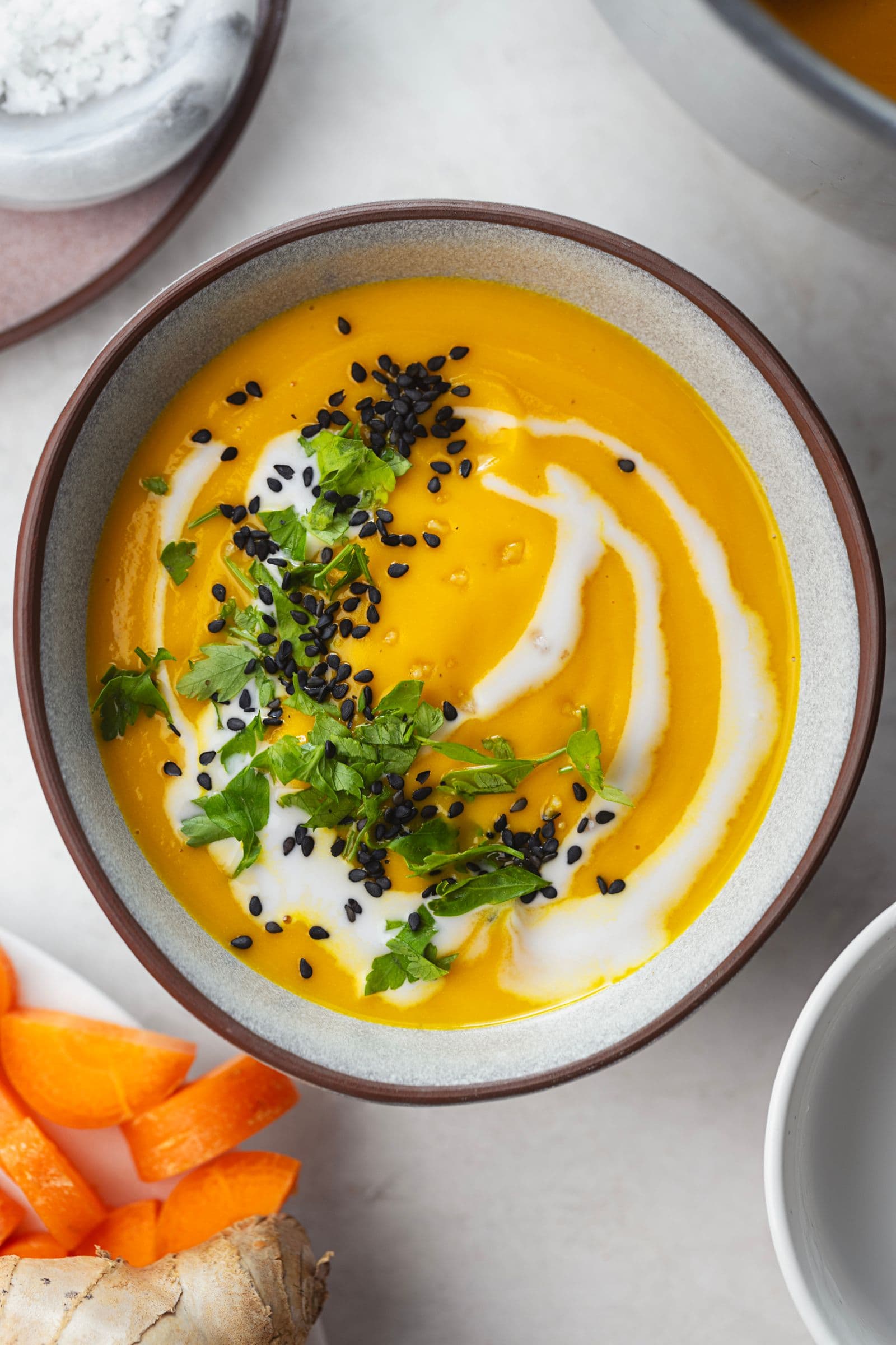Close-up of silky carrot soup topped with coconut milk, fresh herbs, and toasted seeds.