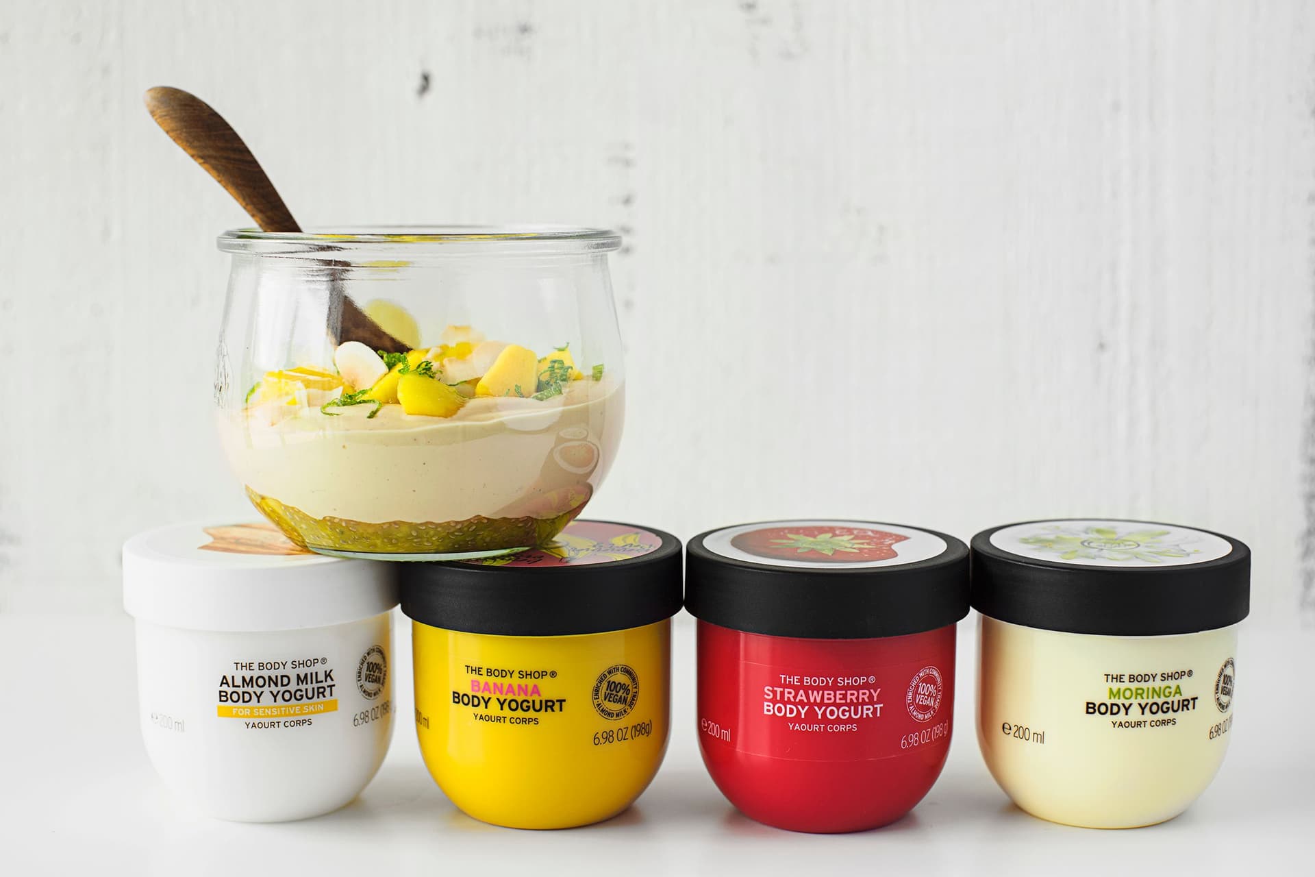 Iogurte vegan de caju e manga servido em frasco de vidro, acompanhado por frascos de iogurte corporal da The Body Shop.