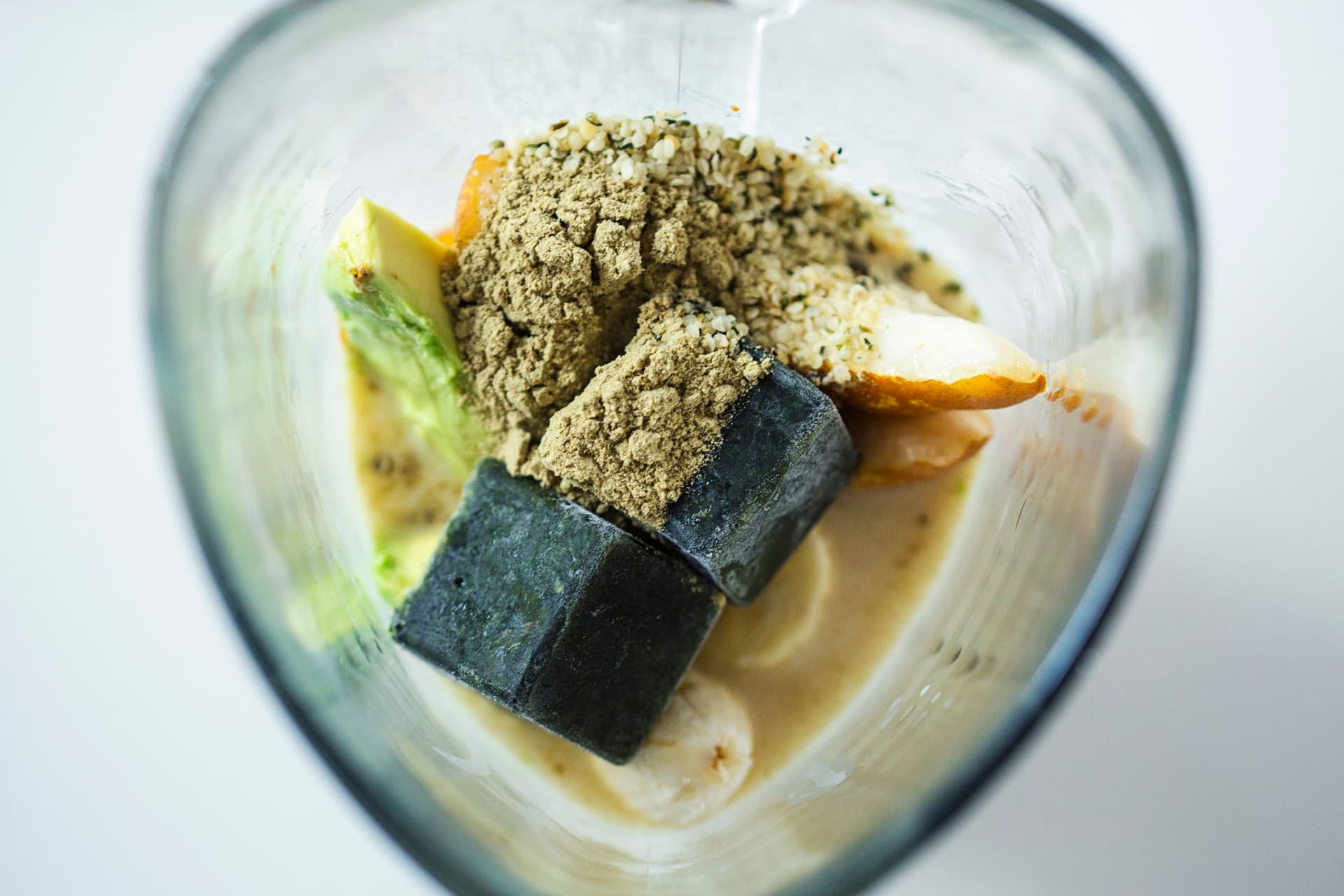 Blender jug with banana, pear, frozen greens cube and hemp seeds.