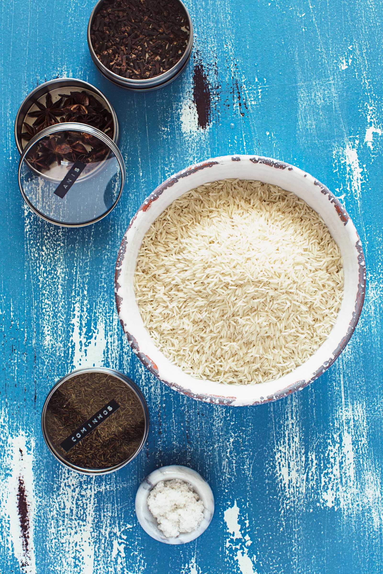 Flat lay of dry basmati rice, spices and salt on a blue surface ready for cooking.
