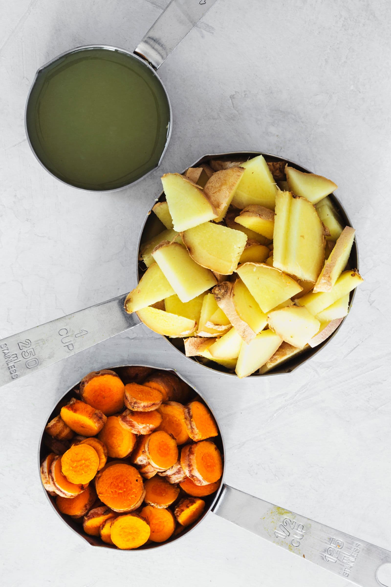 Medidores com gengibre, curcuma fatiada e sumo de limão prontos para triturar.