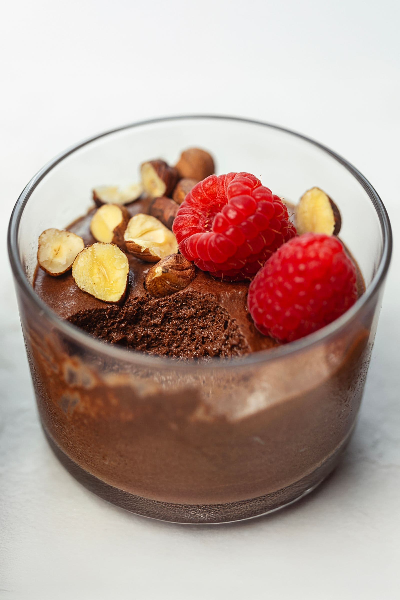 Close-up of vegan chocolate mousse in a glass cup topped with raspberries and nuts.