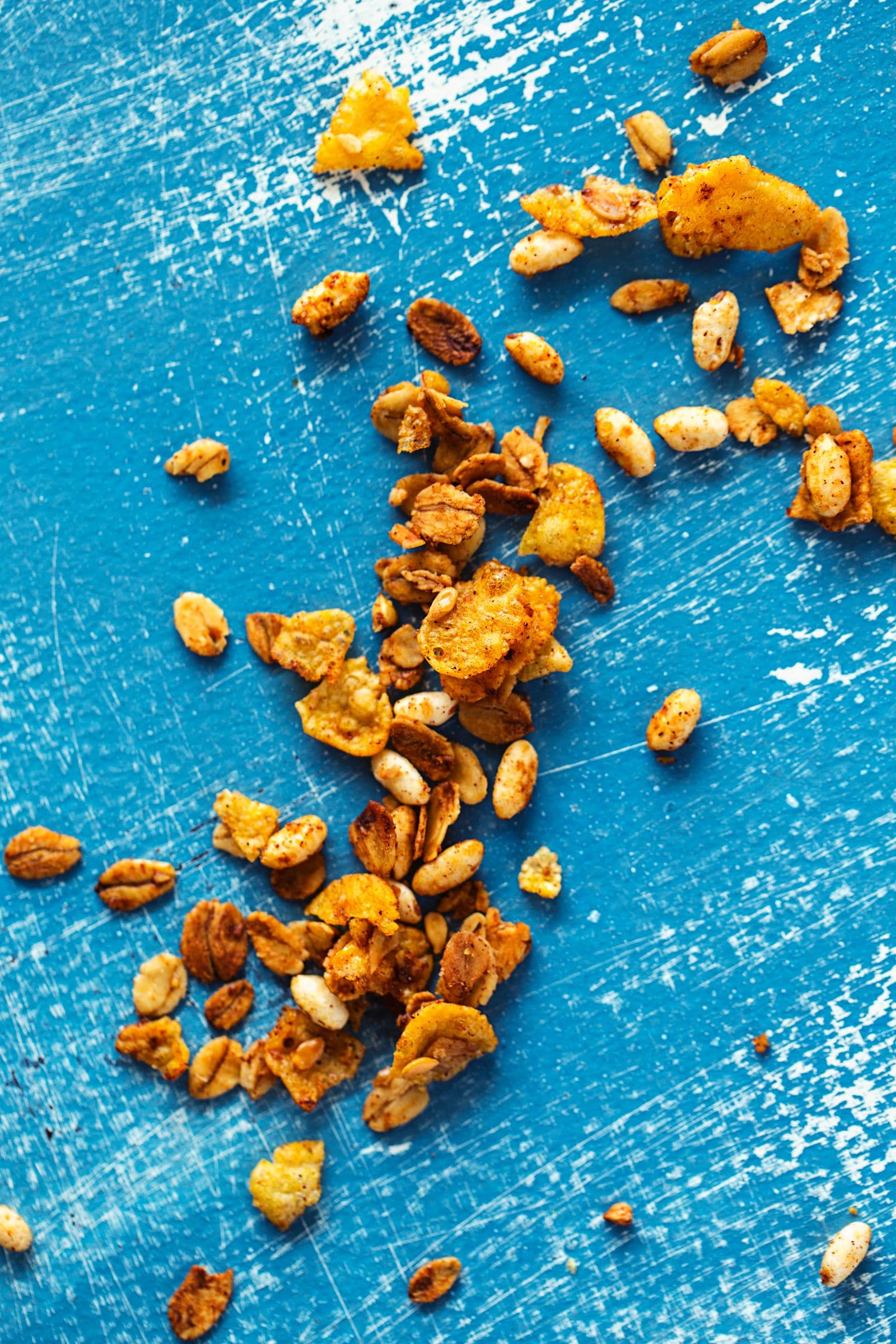 Pedaços de granola dourada com cornflakes espalhados sobre uma mesa azul.