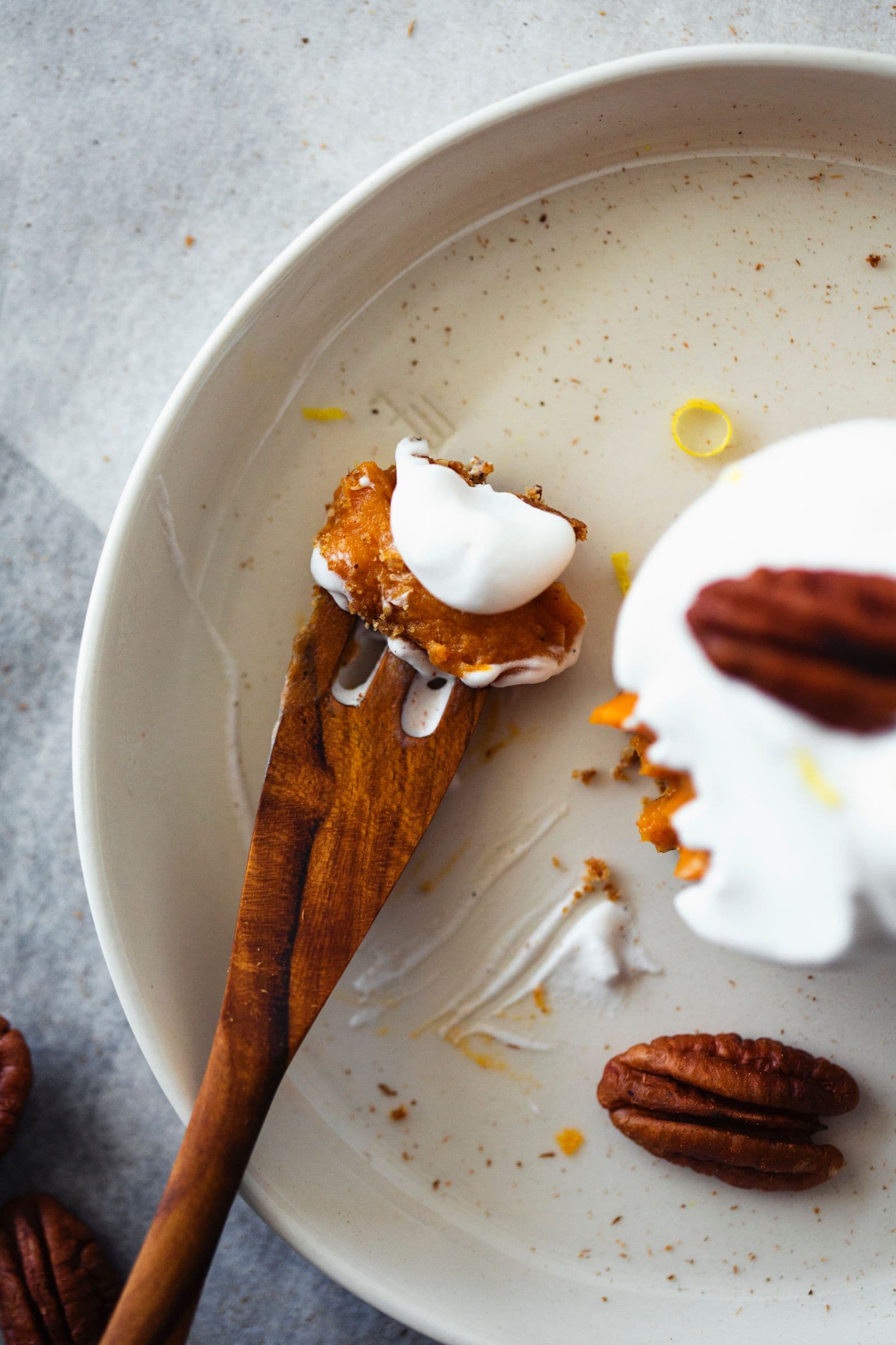 Vista aproximada de fatia de tarte de batata-doce parcialmente comida, com chantilly, noz pecan e migalhas no prato.