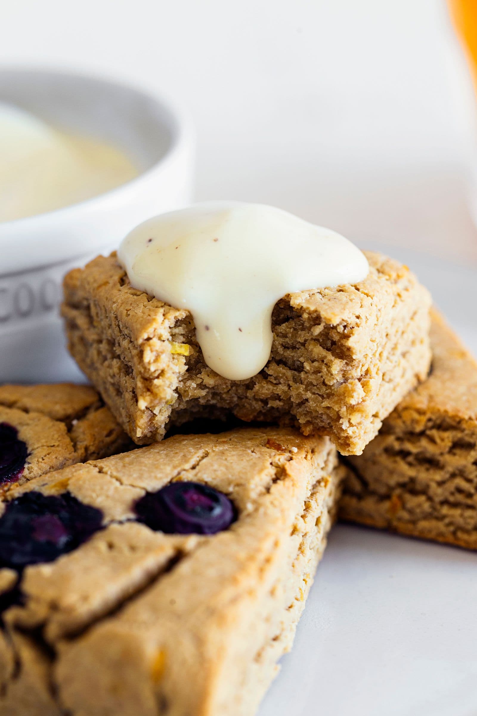 Scone vegano de limão e mirtilos com creme, já com uma dentada, num prato.