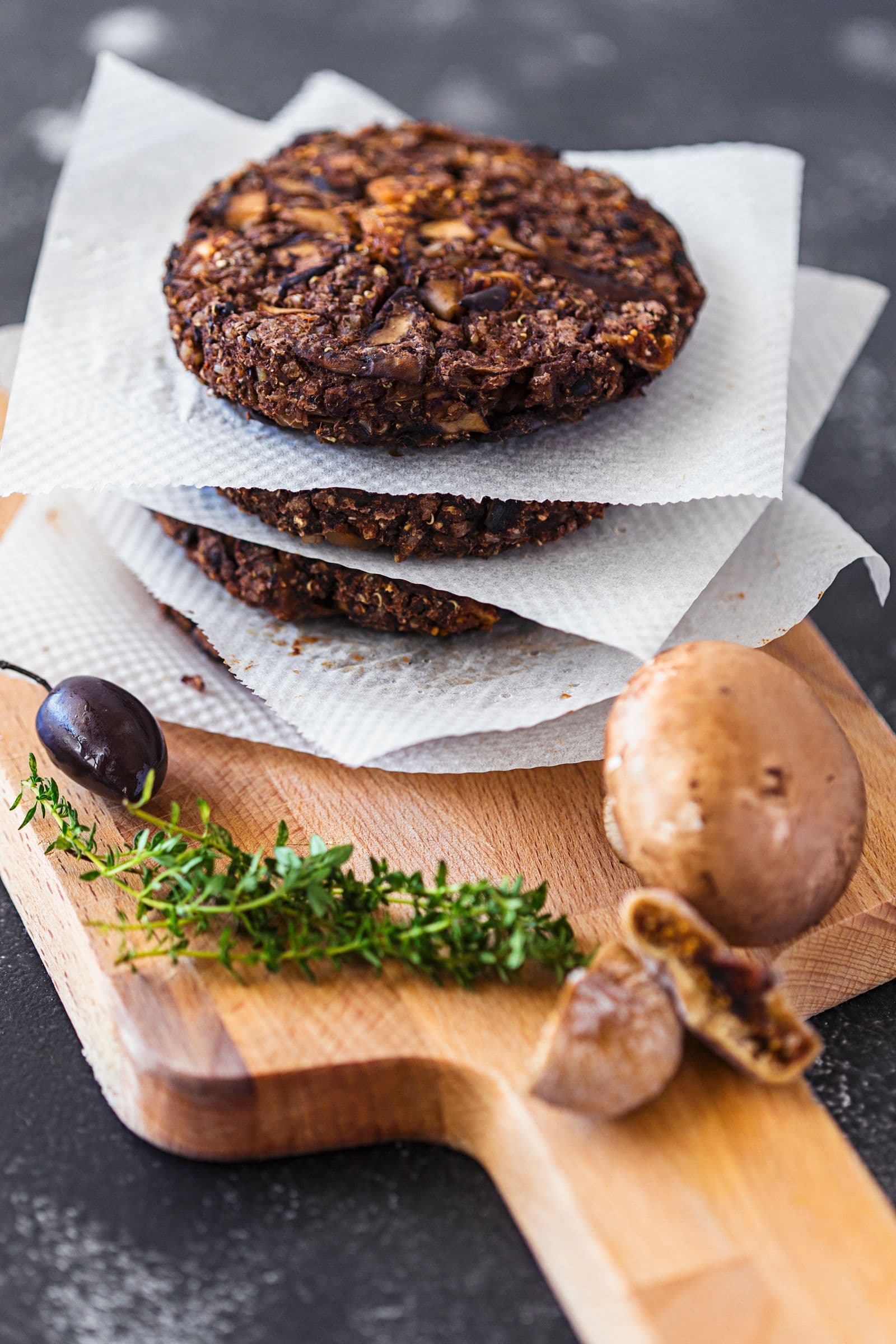 Stack of black bean burger patties on parchment paper with fresh herbs and mushrooms.