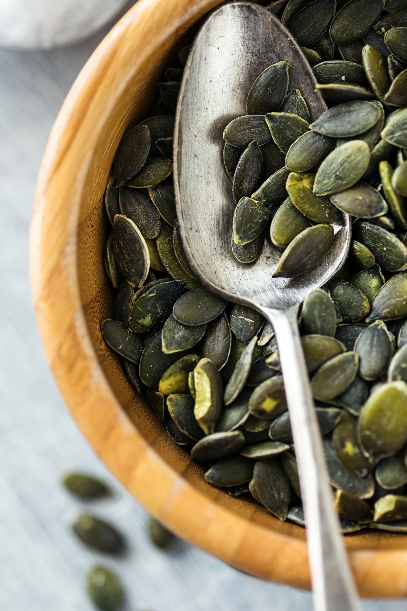 Wooden bowl with pumpkin seeds and a spoon.