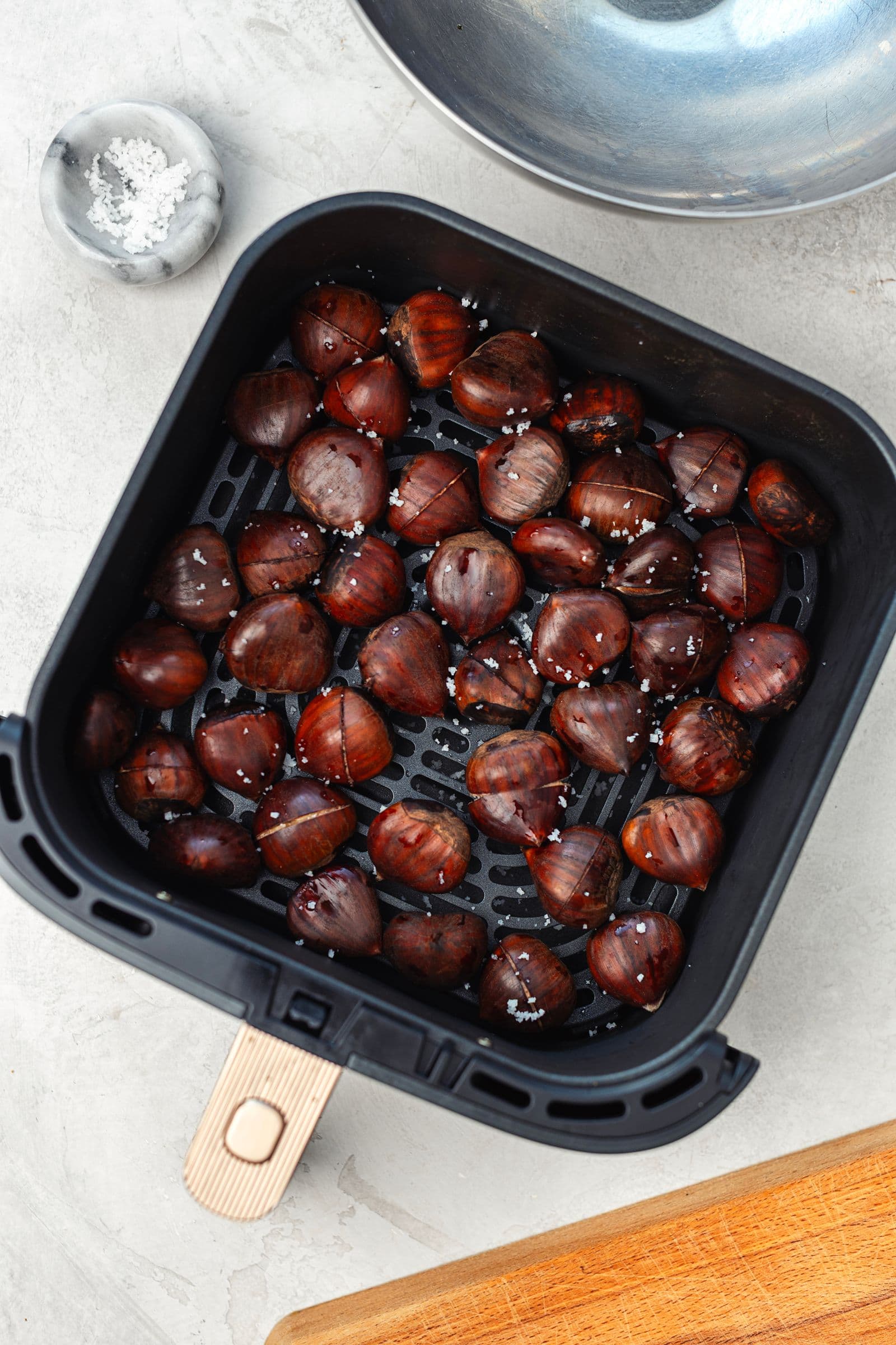 Castanhas escorridas dentro do cesto da air fryer, polvilhadas com sal grosso antes de assar.