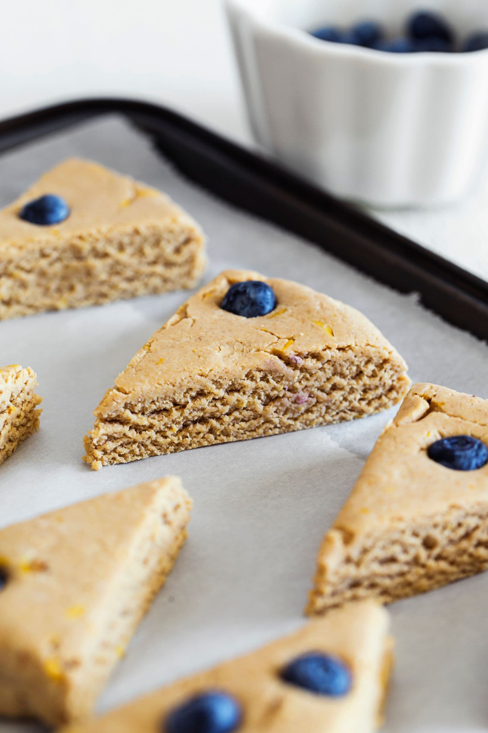 Scones veganos de limão e mirtilos crus, espaçados num tabuleiro forrado com papel vegetal antes de cozer.