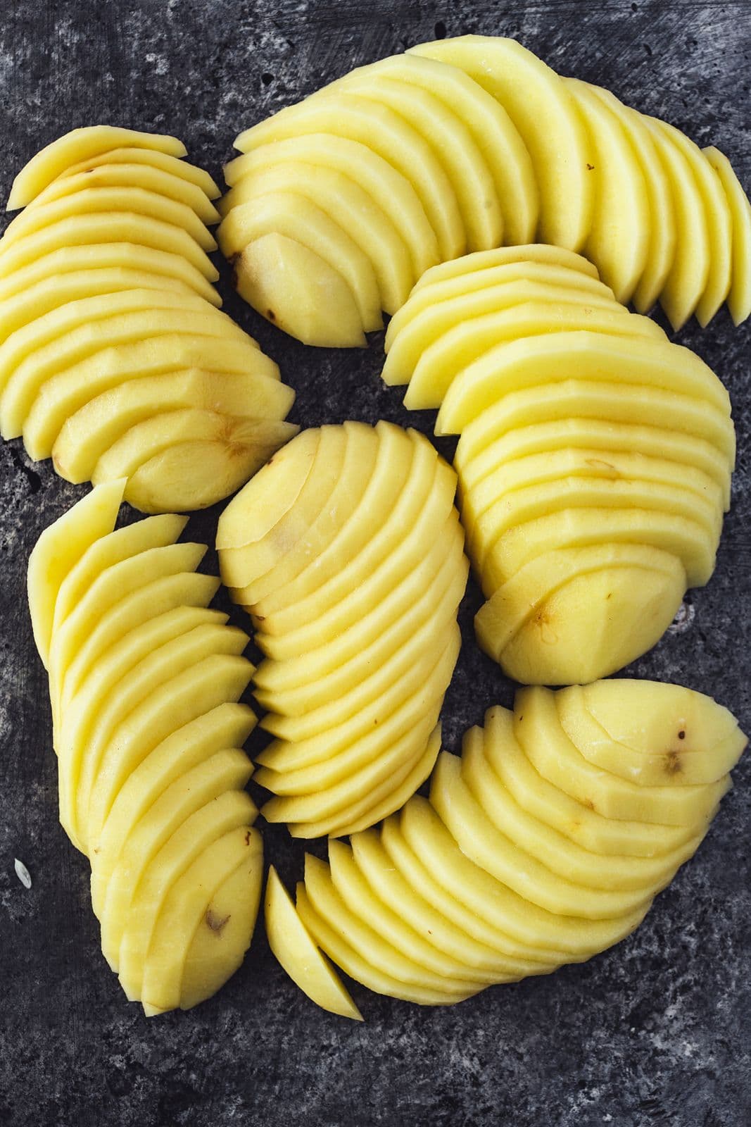 Batatas cortadas em fatias finas, dispostas em filas sobre fundo escuro.
