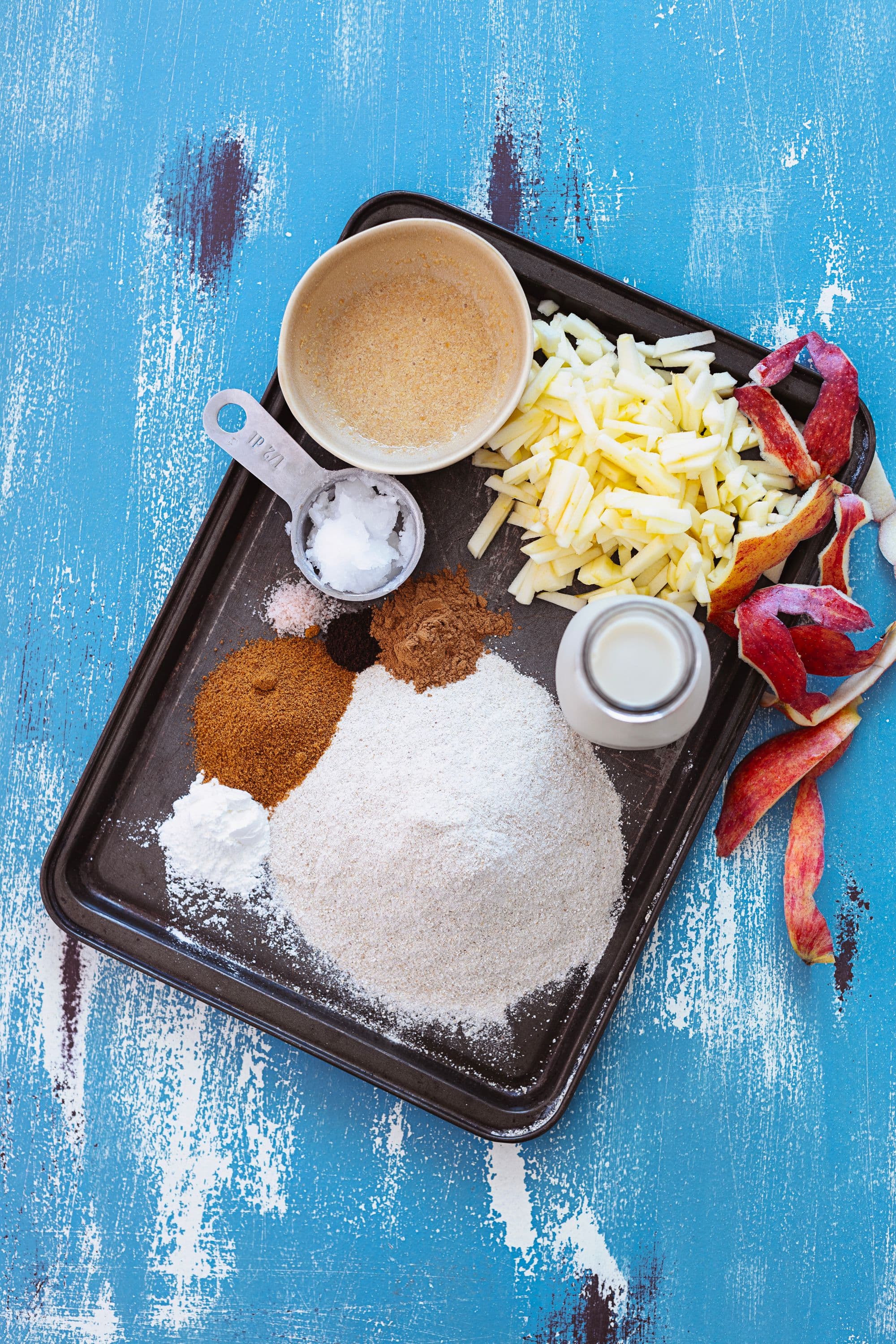 Flat lay of pancake ingredients including chopped apple, buckwheat flour, coconut sugar and spices.