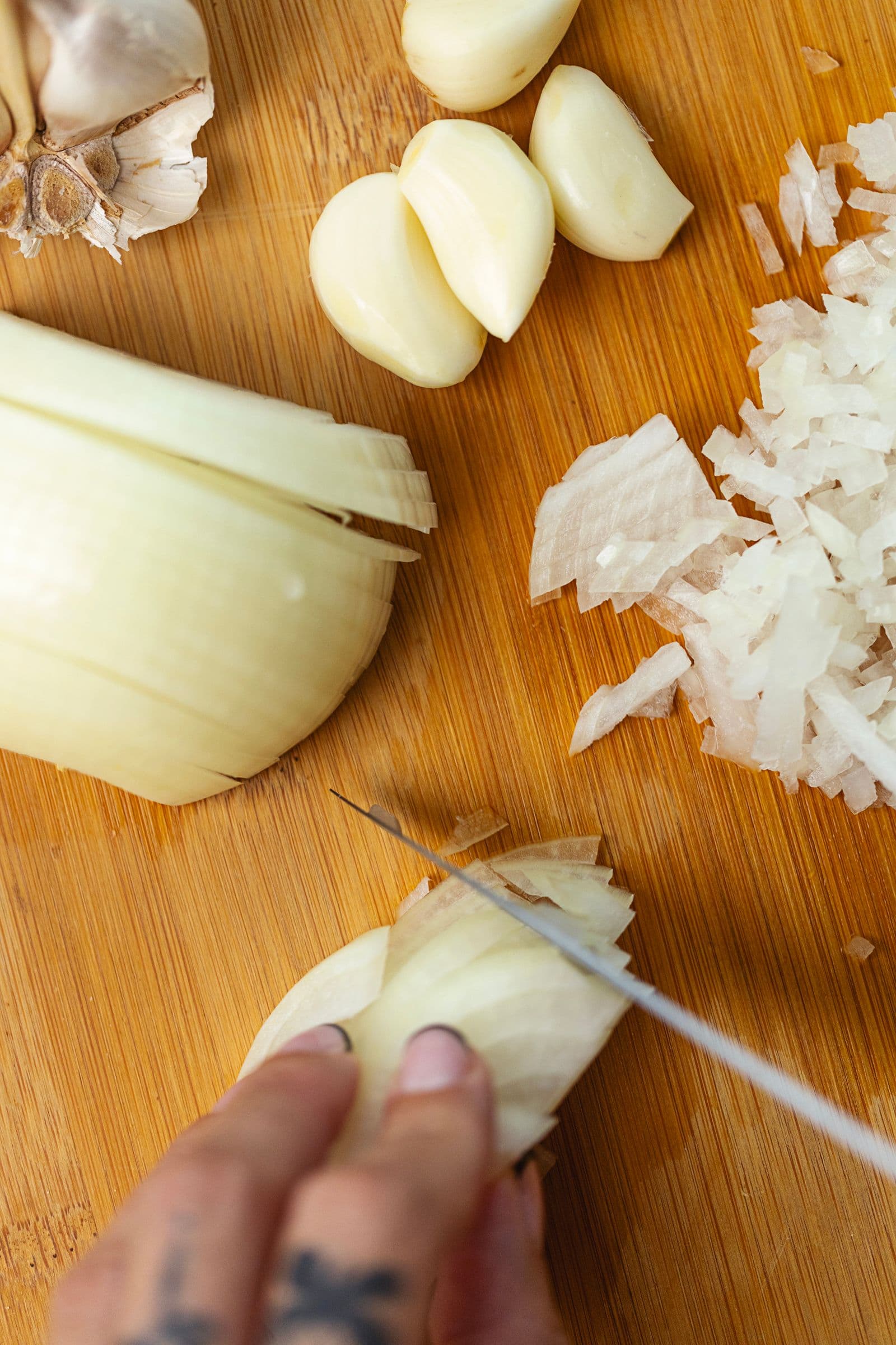 Close-up of onion and garlic being finely chopped on a wooden board.