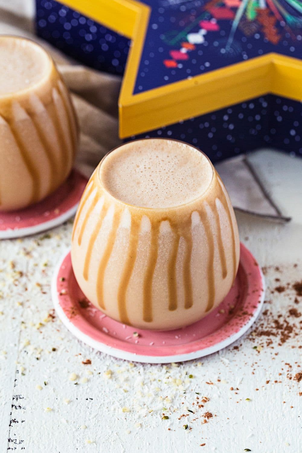 Rounded glass with salted caramel and peanut butter smoothie, drizzled with caramel sauce, on a pink coaster.