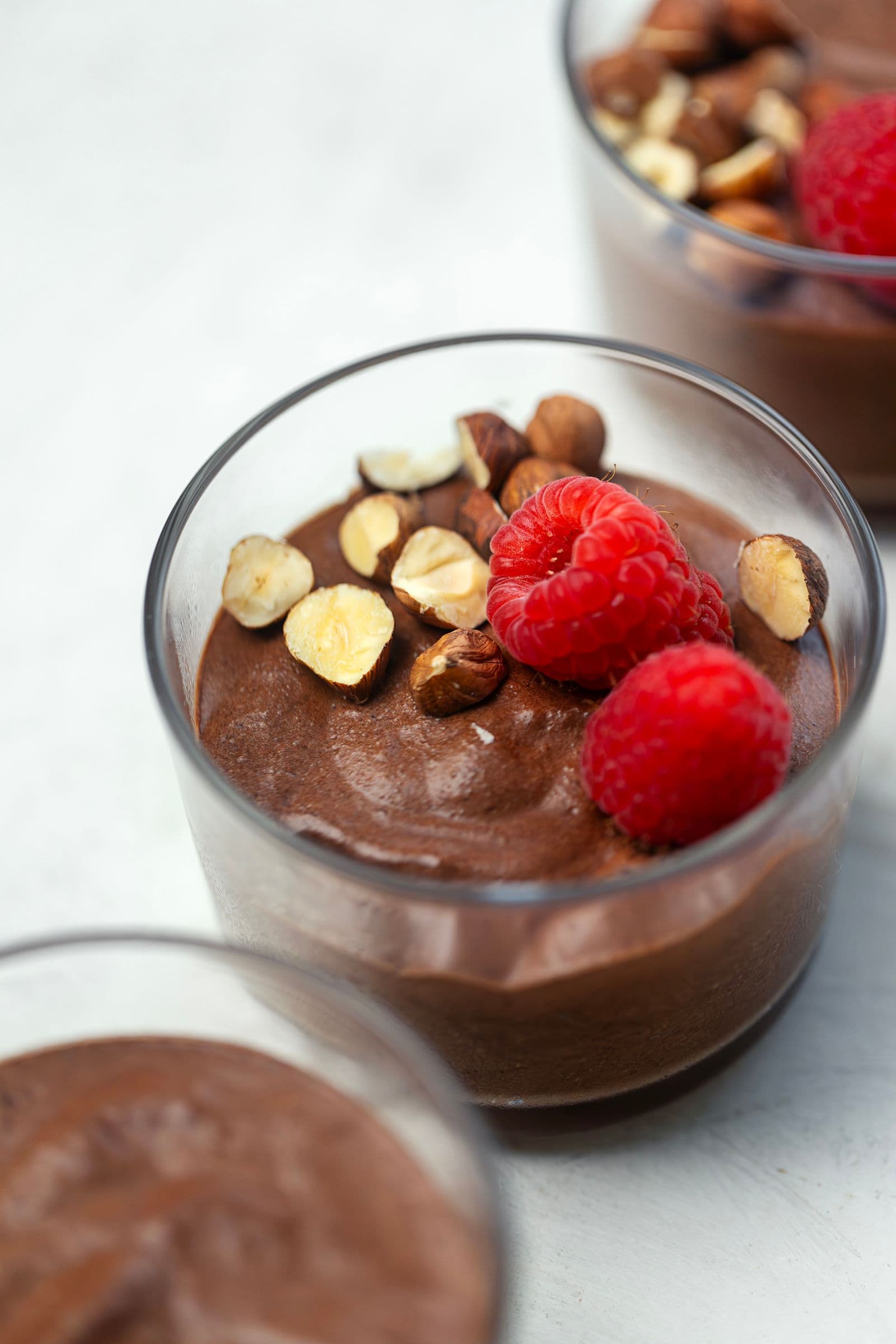 Close-up de mousse de chocolate vegan num copo de vidro, com framboesas e frutos secos.