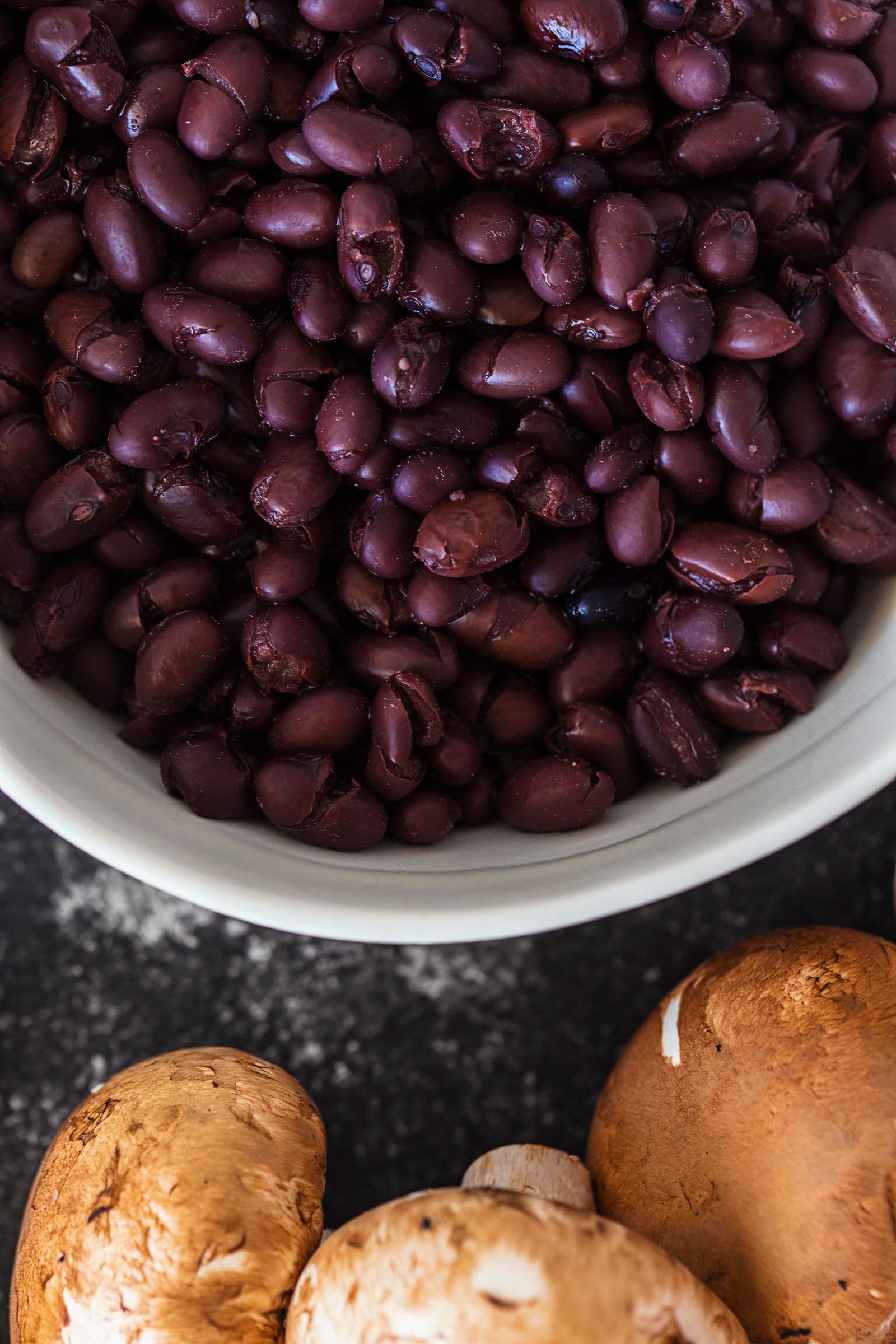 Bowl filled with cooked black beans surrounded by mushrooms.
