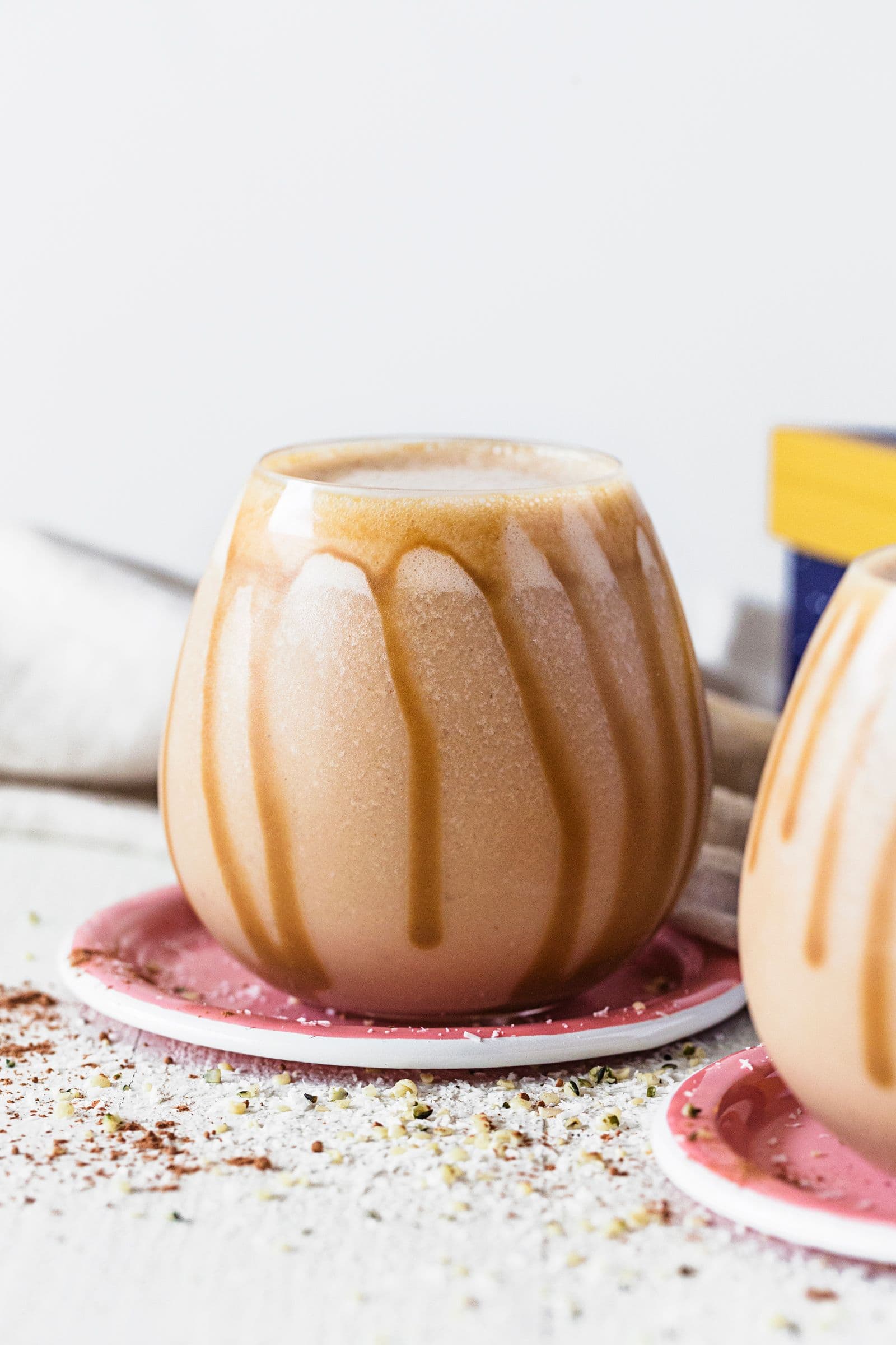 Copo arredondado com smoothie de caramelo salgado e manteiga de amendoim, servido em base cor-de-rosa, com fio de caramelo escorrido pelas laterais.