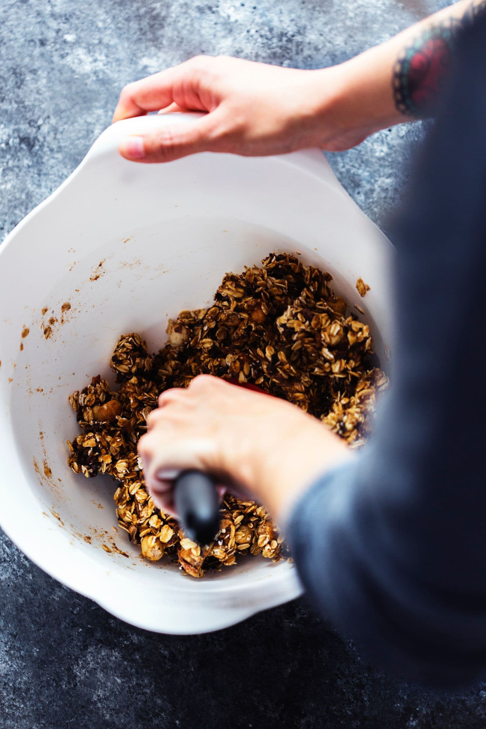Mãos a misturar a massa pegajosa da granola numa taça branca.