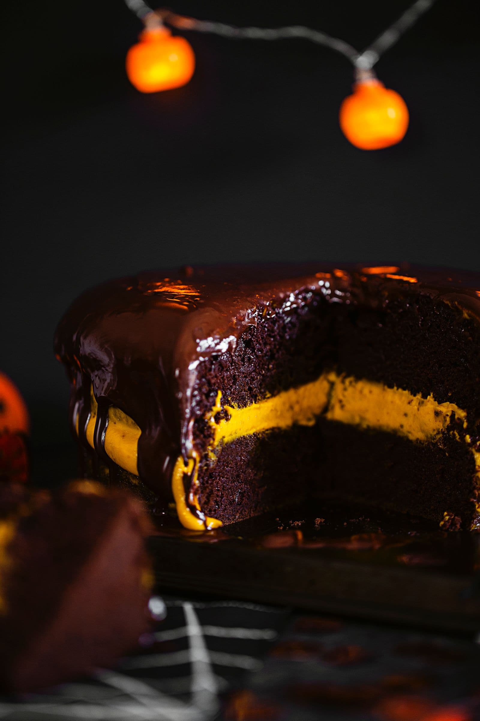 Close-up of a moist chocolate cake with orange creamy filling and shiny chocolate glaze on top.