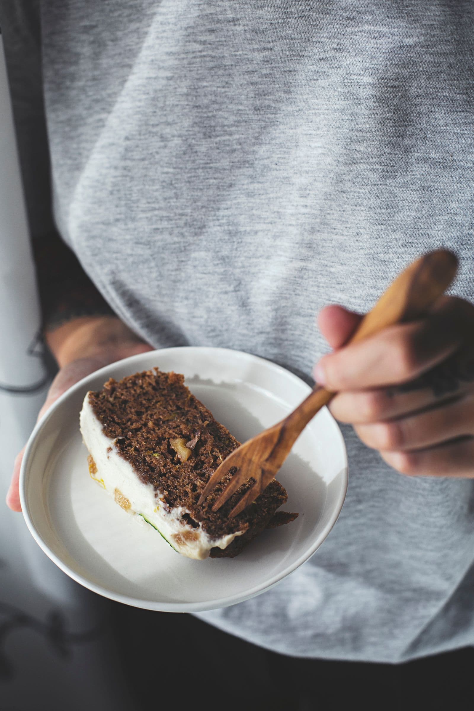 A hand holding a fork with a bite of zucchini and lemon cake.