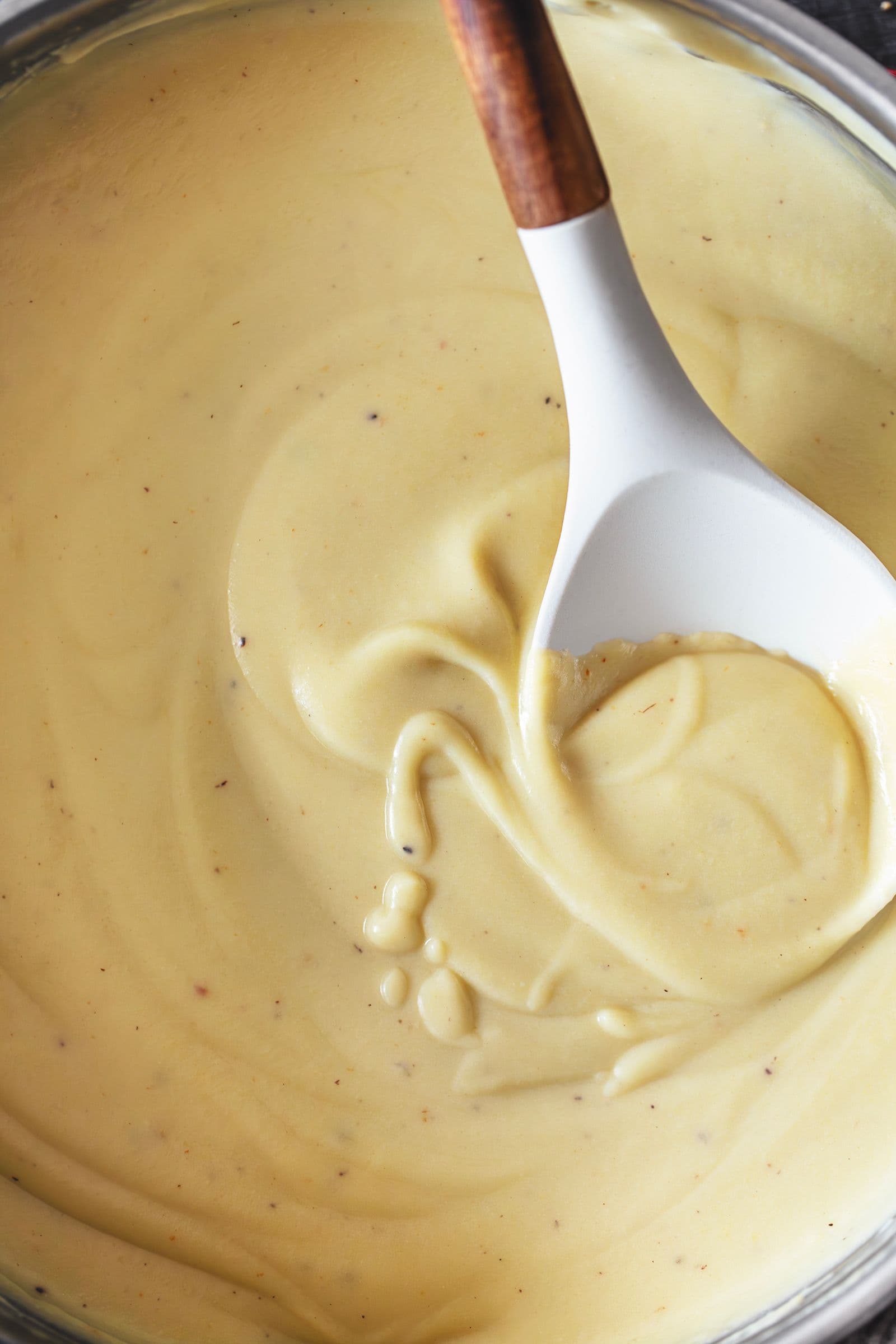 Molho béchamel vegan e sem glúten, cremoso e aveludado, numa panela com colher branca de cabo em madeira
