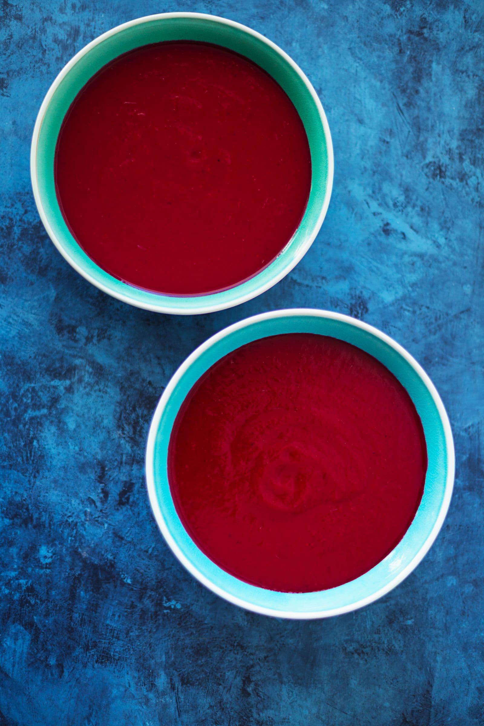 Two bowls filled with smooth beetroot soup, without toppings yet.