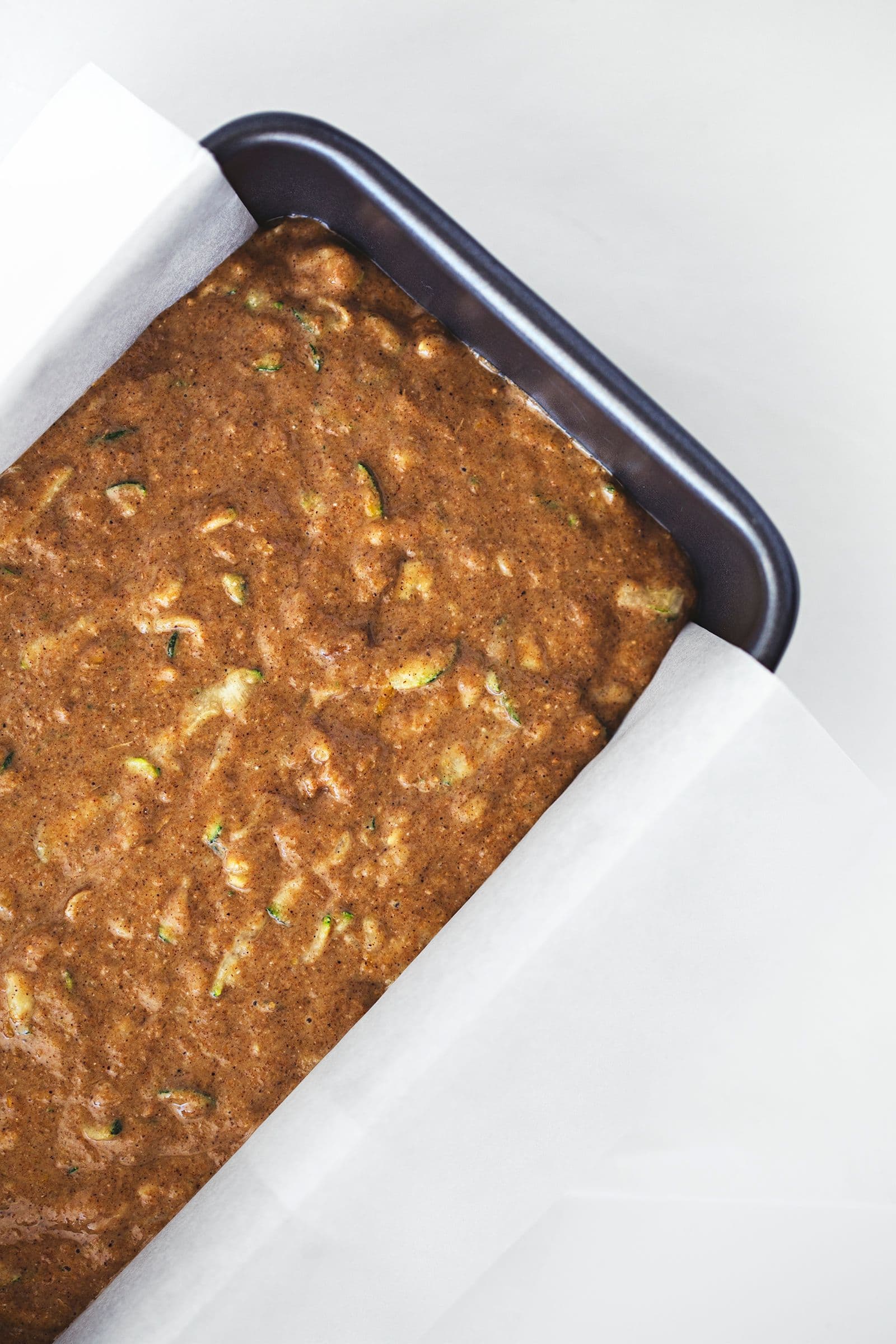 Massa de bolo de curgete espalhada uniformemente numa forma forrada, pronta para ir ao forno.