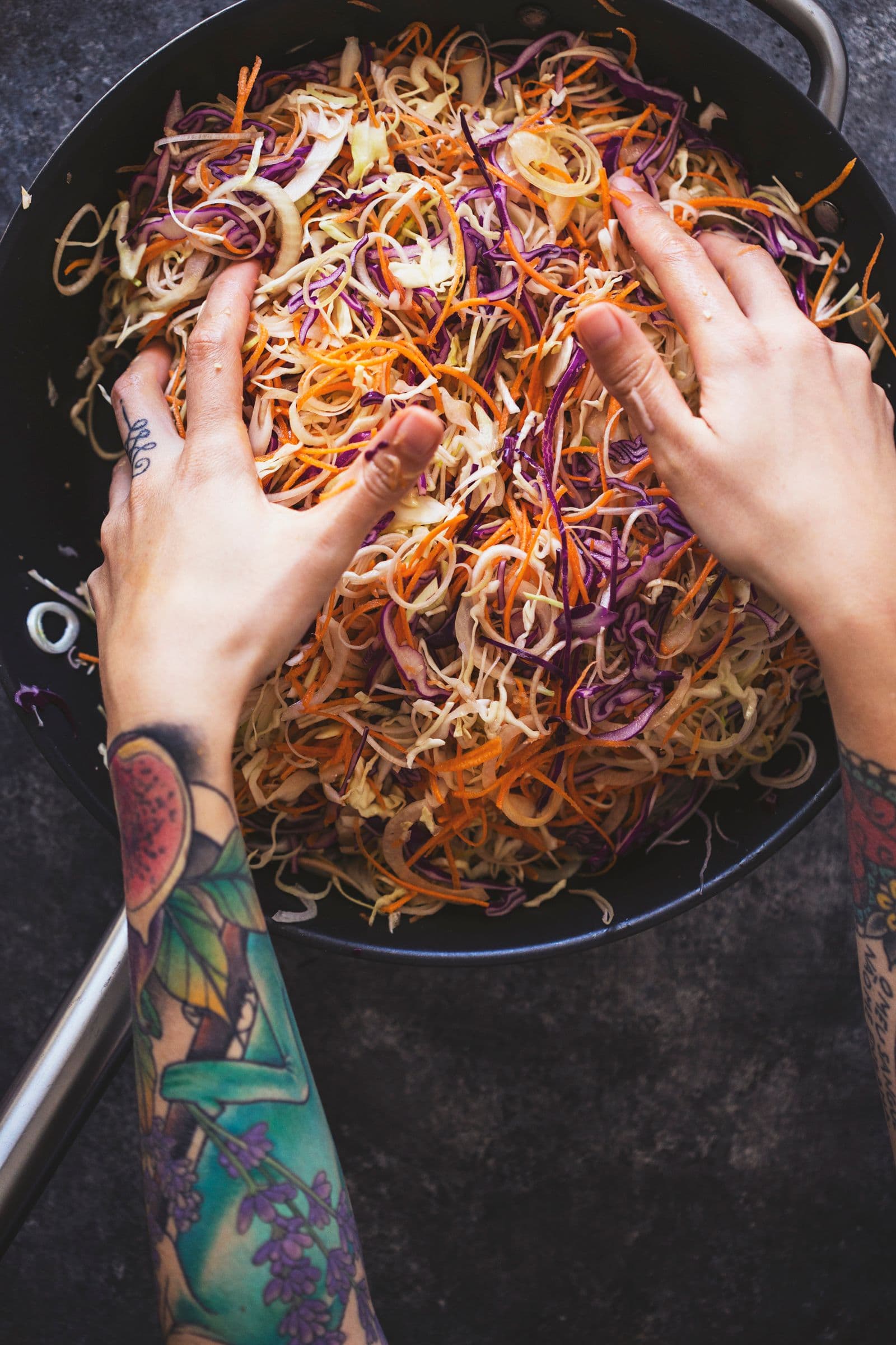 Hands stirring thinly sliced vegetables in a pan before sautéing.