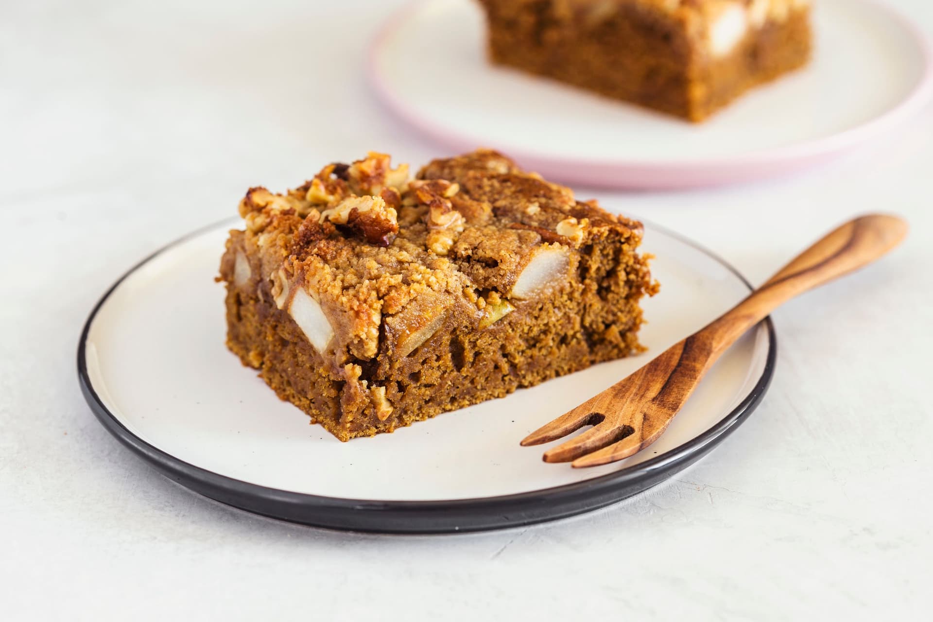 A slice of vegan coffee and pear coffee cake on a white plate with a wooden fork.