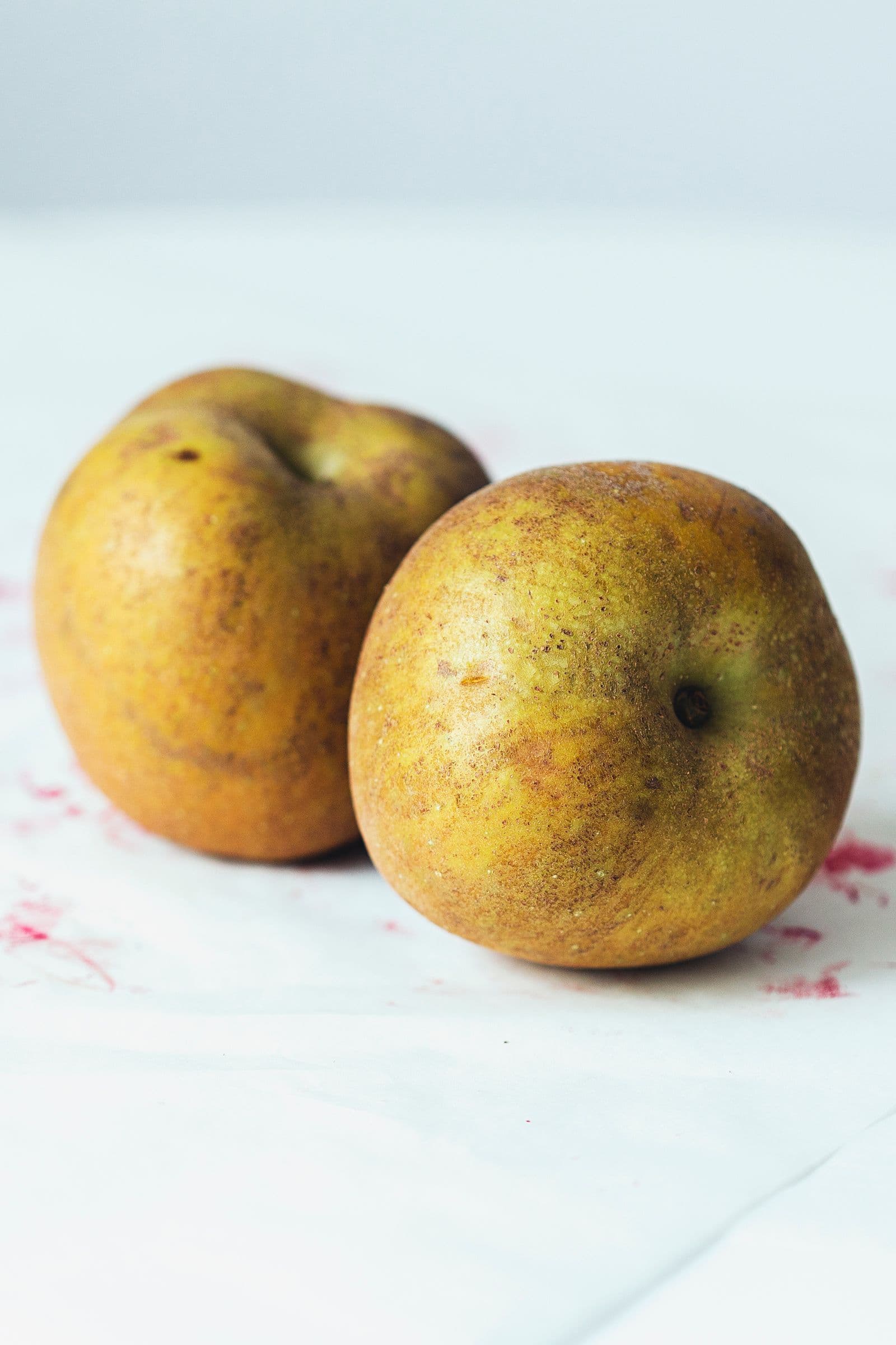 Two ripe reinette apples sitting on white parchment paper.