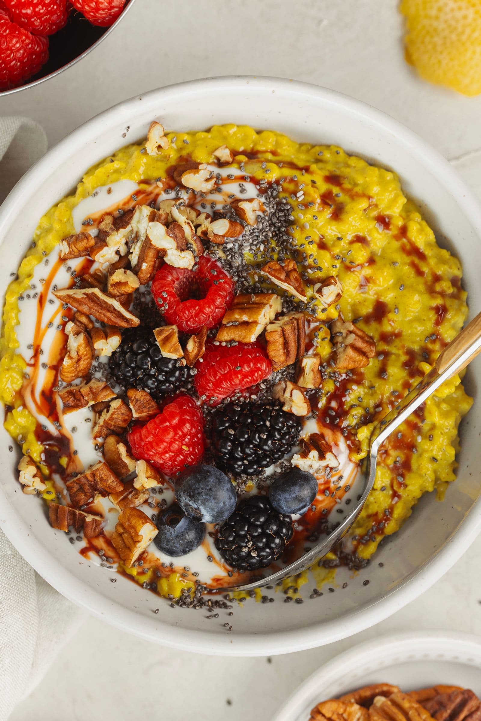 Golden oatmeal with chia, pecans, berries, plant yogurt and date syrup, served in a white bowl with a spoon