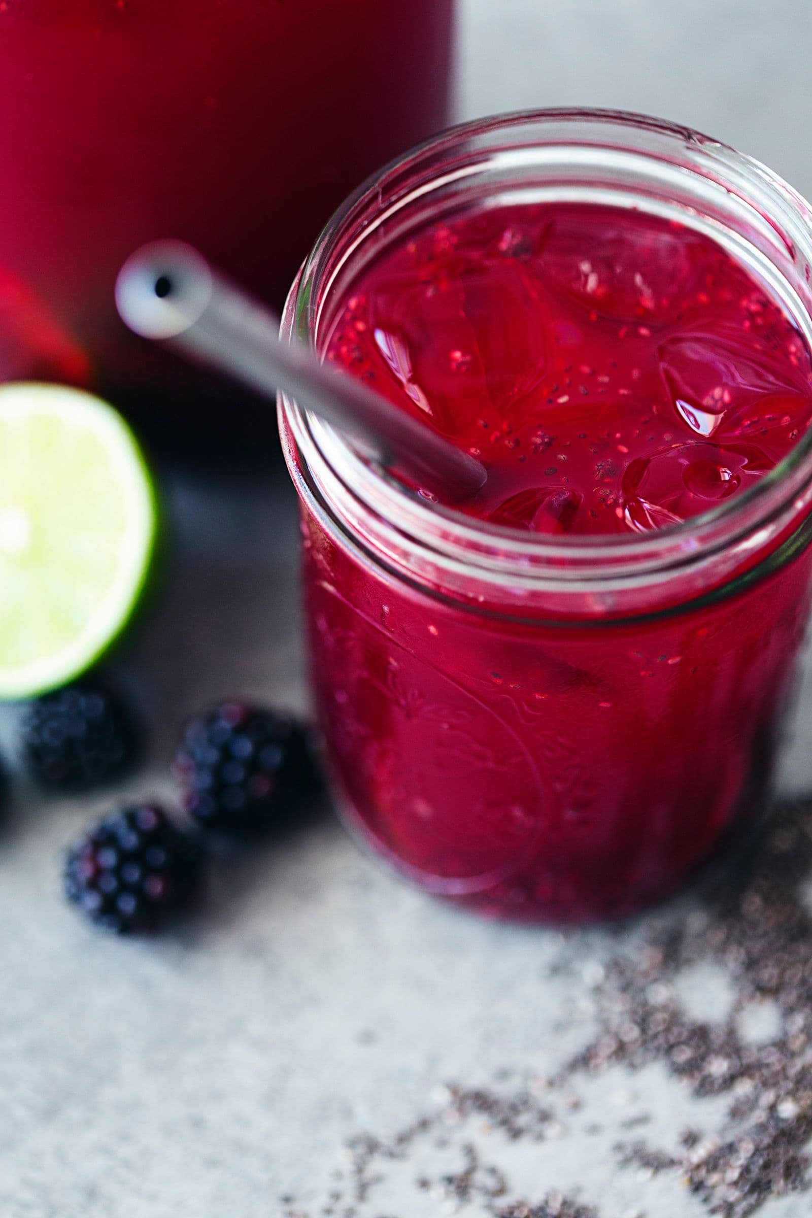 Glass of chia fresca with ice, lime wedge, blackberries and a straw.