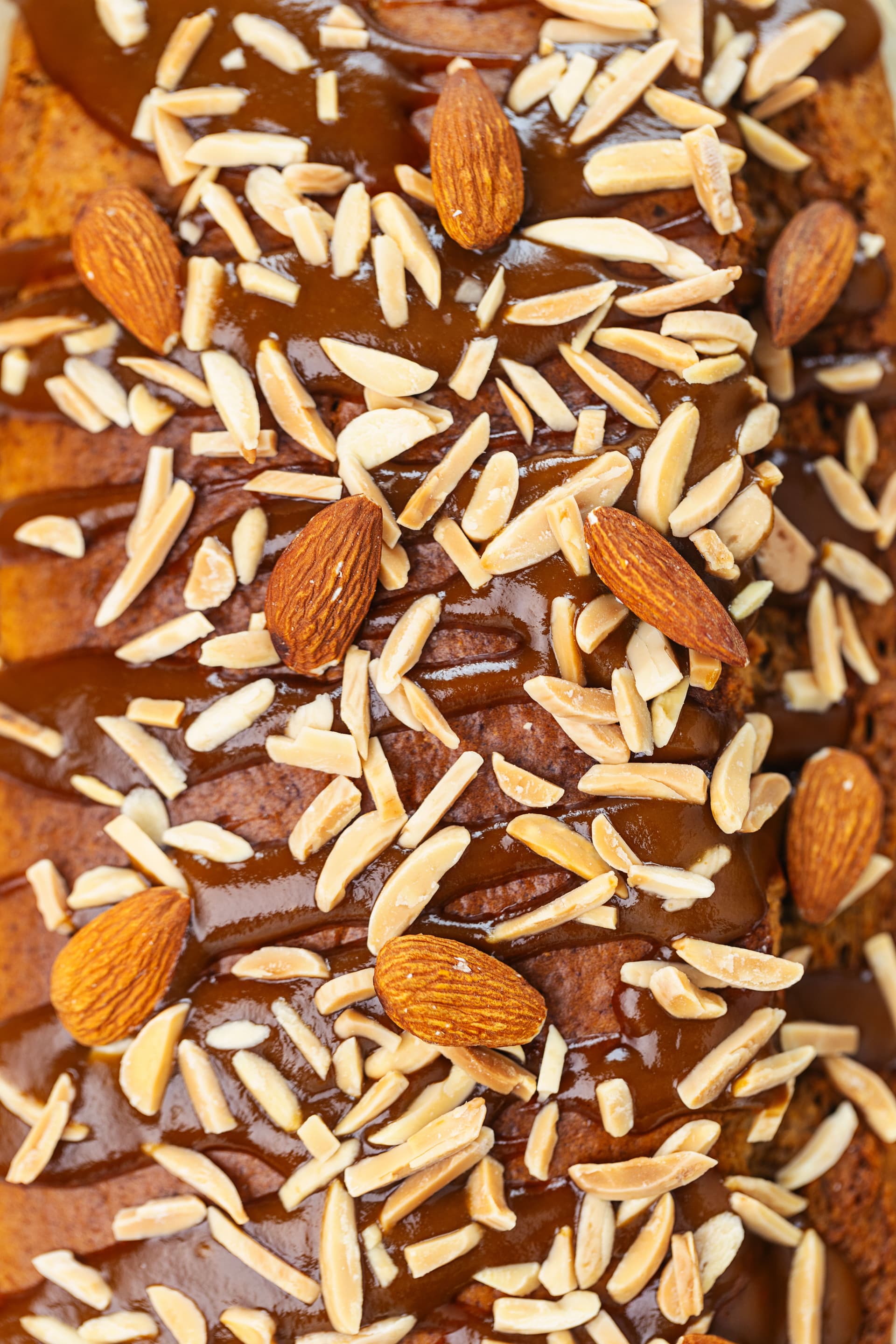 Overhead close-up of the almond cake top with glossy coconut caramel and a scatter of slivered and whole almonds.