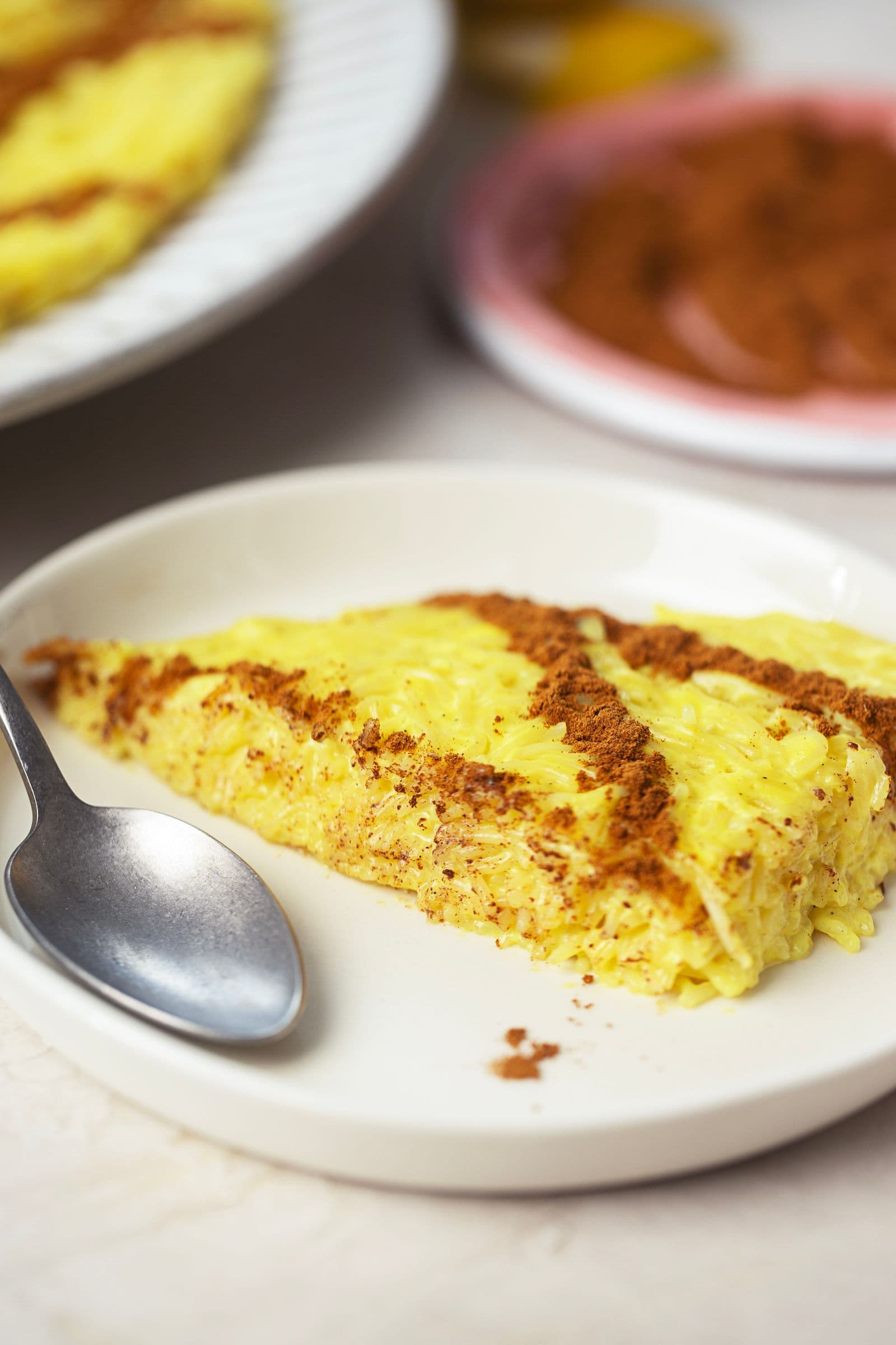 Close-up of a creamy slice of vegan Aletria, showing its texture and cinnamon decoration, served on a white plate.