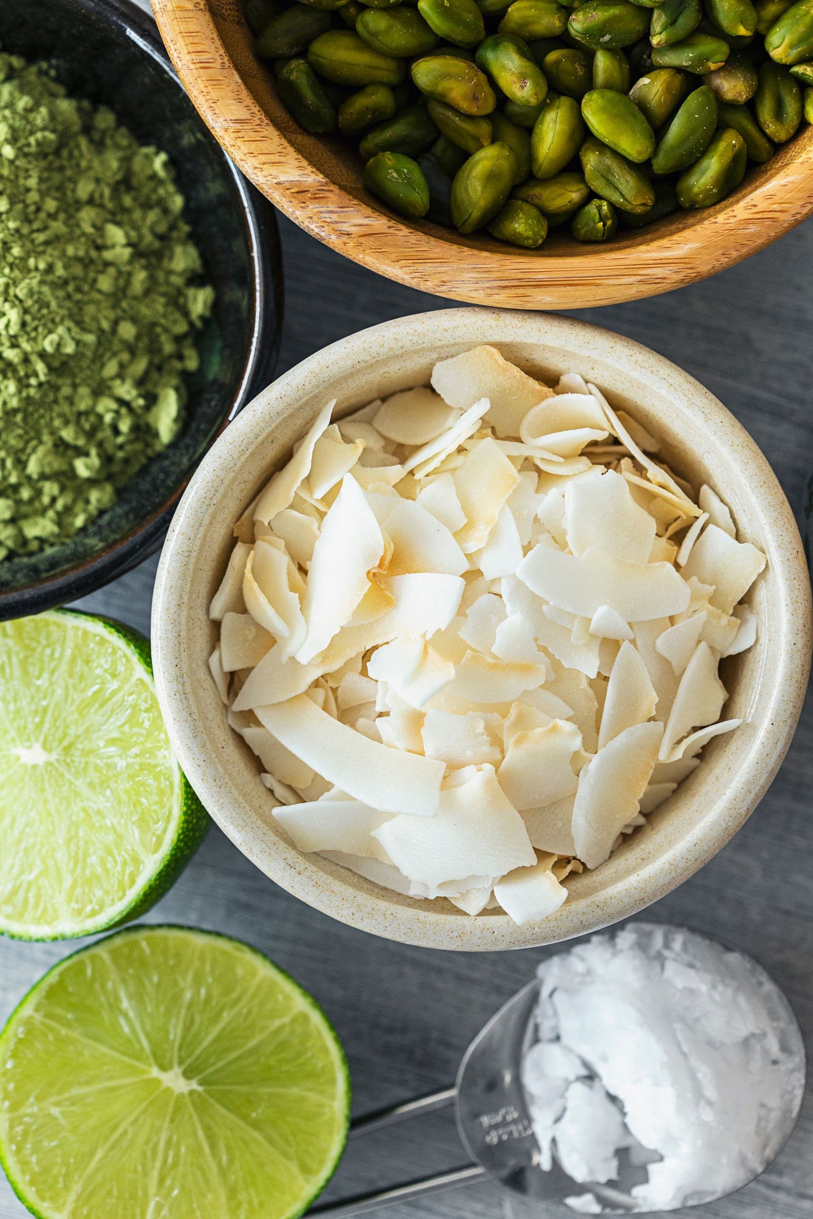 Bowls and spoons with coconut flakes, lime slices, coconut oil, wheatgrass powder and pistachios.