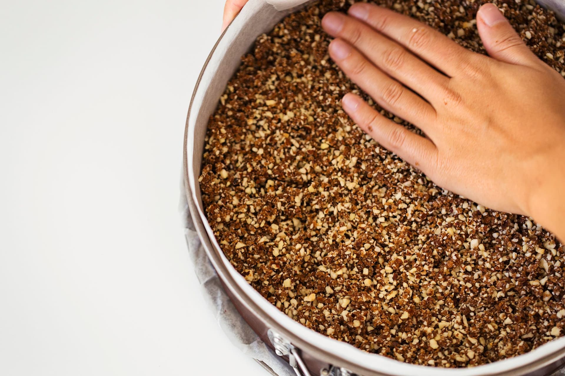 Mão a pressionar a base do cheesecake numa forma de aro removível.