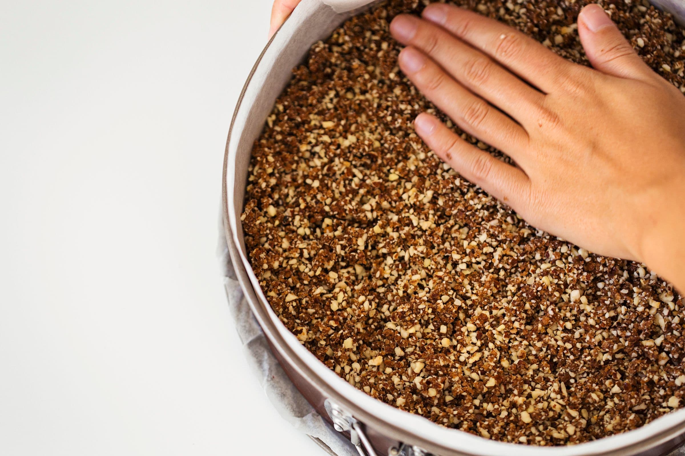 Hand pressing down crust mixture into a springform pan.