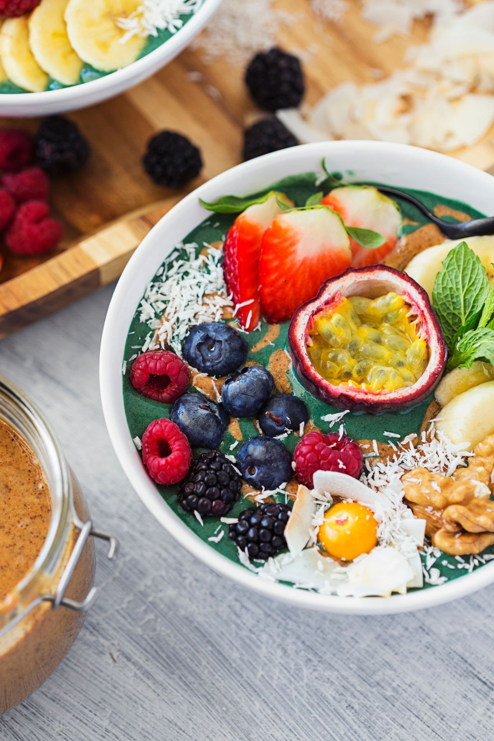 Taça de smoothie de spirulina com toppings coloridos: fruta, frutos secos e coco ralado.