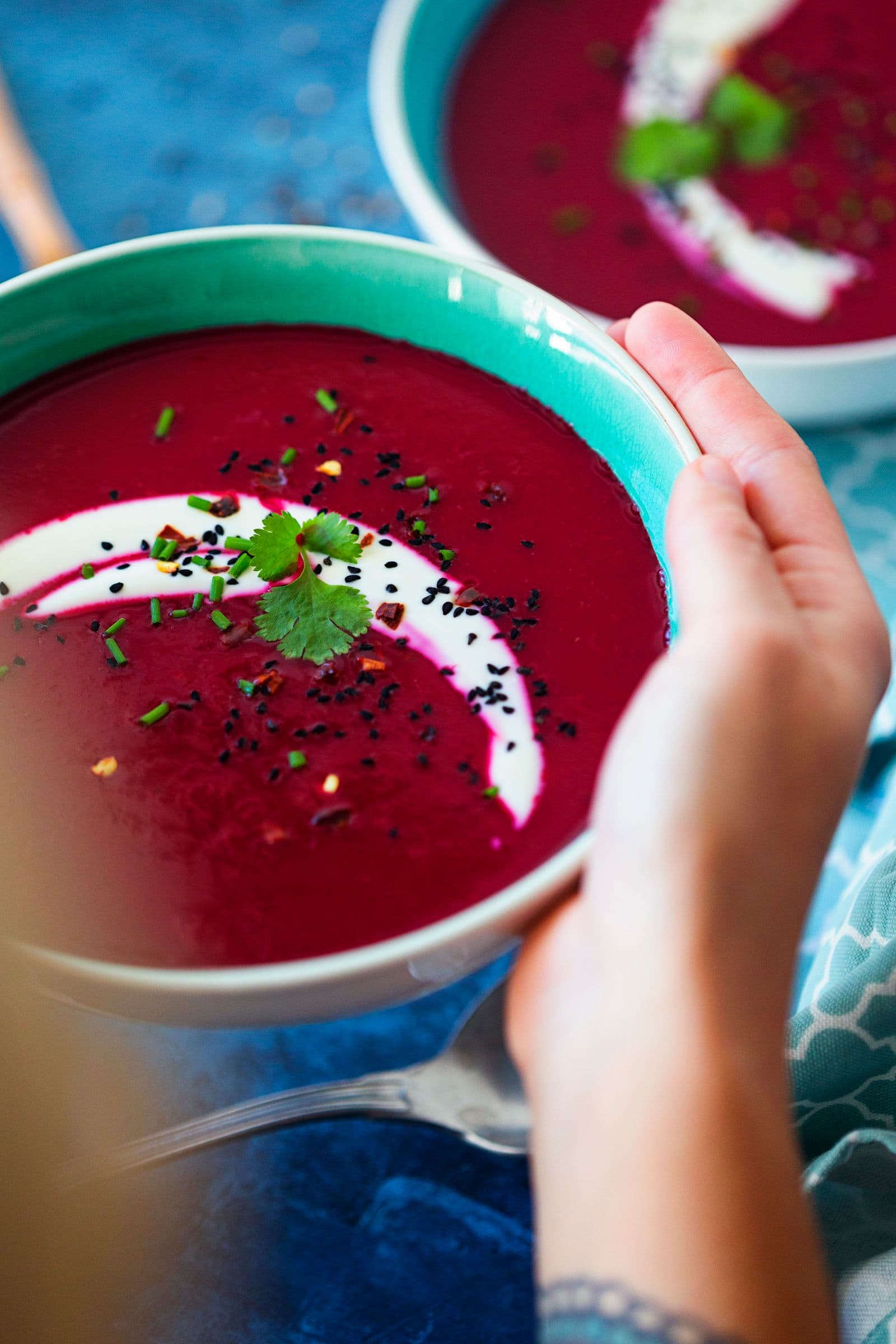 Hands holding a bowl of beetroot and apple soup, ready to eat.