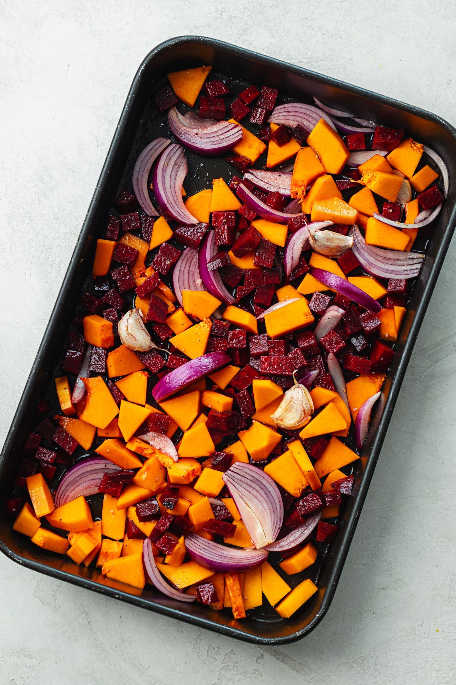 Raw butternut squash, beetroot, red onion and garlic cut into chunks and arranged on a baking tray before roasting.
