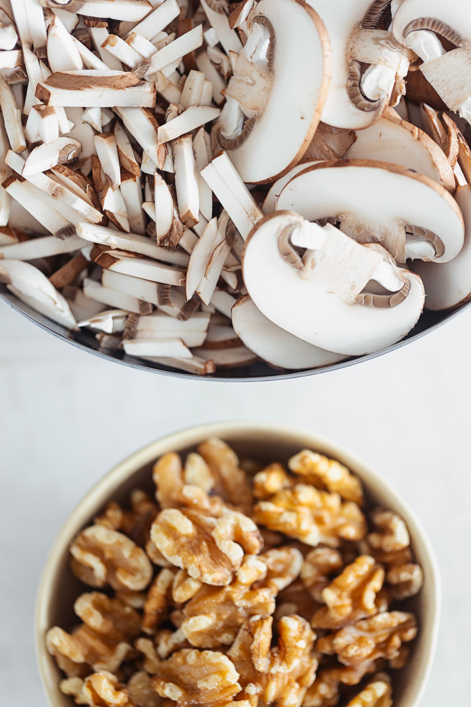 Bowls of whole walnuts and chopped brown mushrooms ready for cooking.