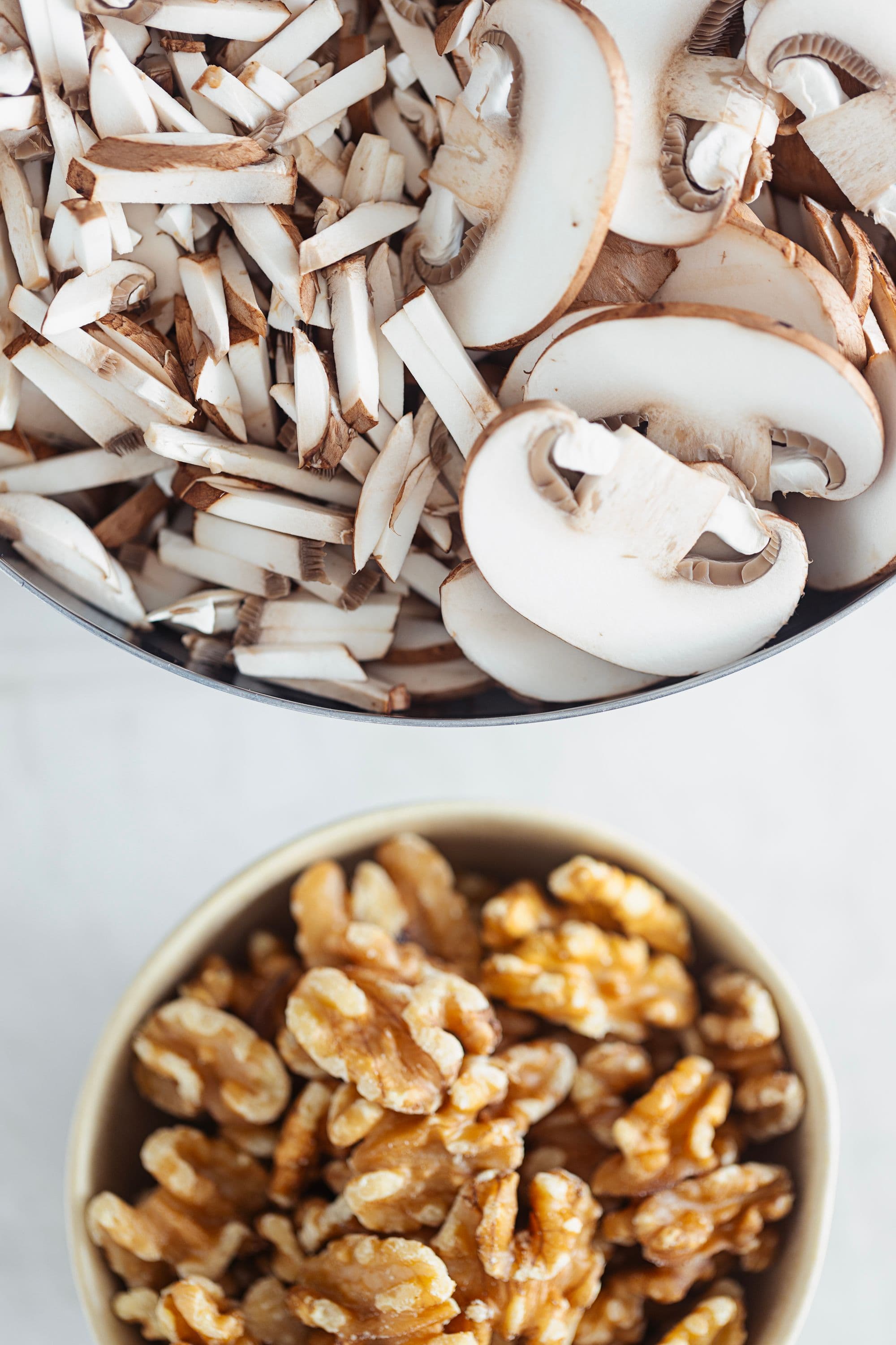 Bowls of whole walnuts and chopped brown mushrooms ready for cooking.