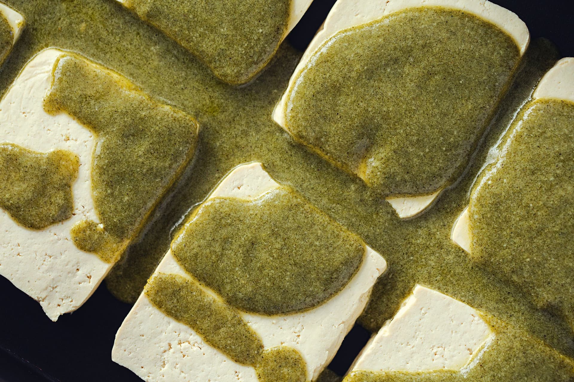 Fatias grossas de tofu cobertas com marinada verde, prontas para assar.