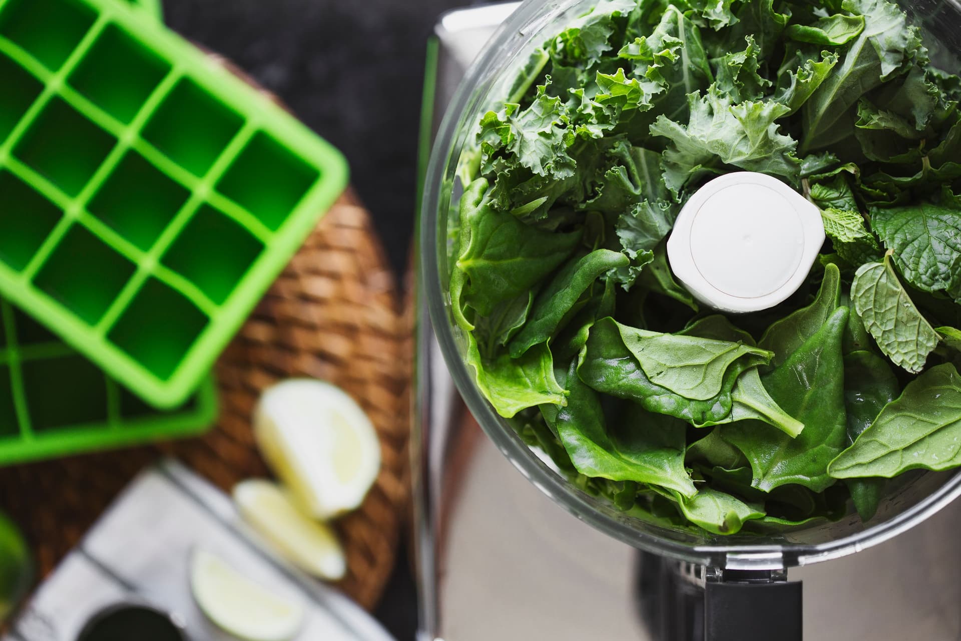 Processador de alimentos cheio de espinafres, couve-kale e hortelã frescos.