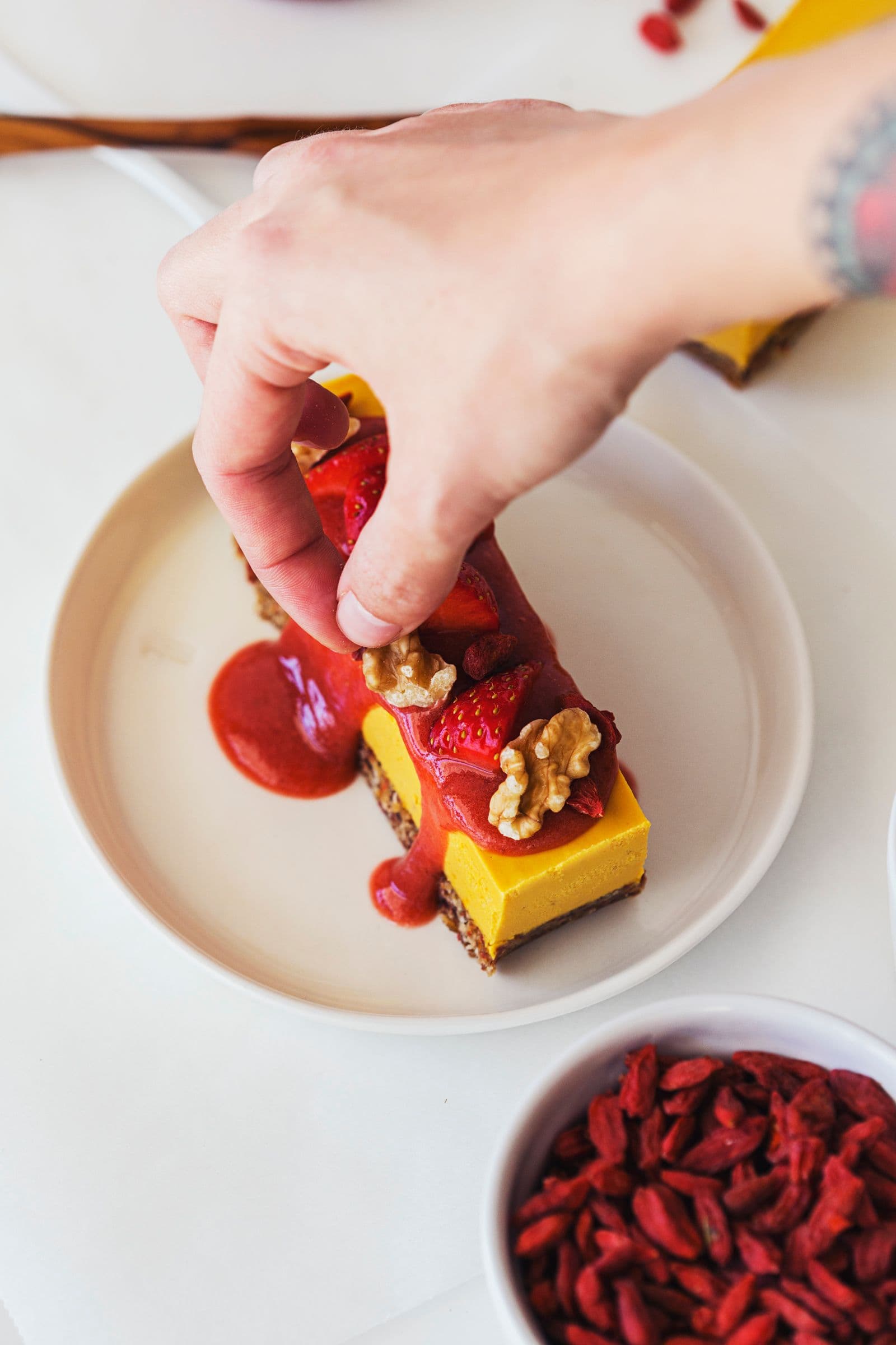 Hand decorating slice of raw vegan cheesecake with walnuts.