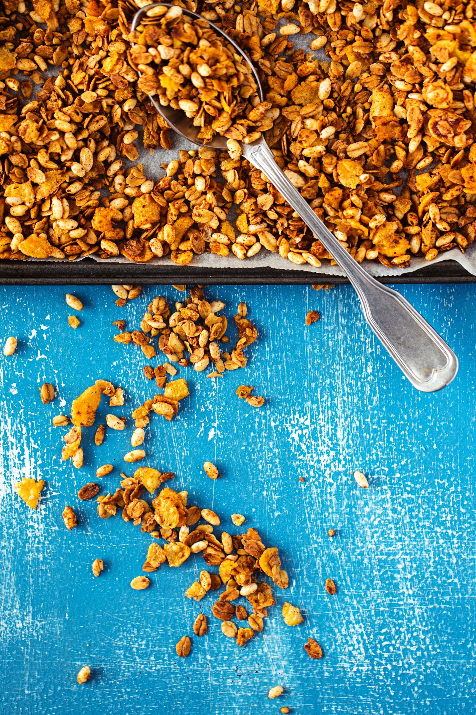 Spoon breaking up baked granola into crunchy clusters on a tray.