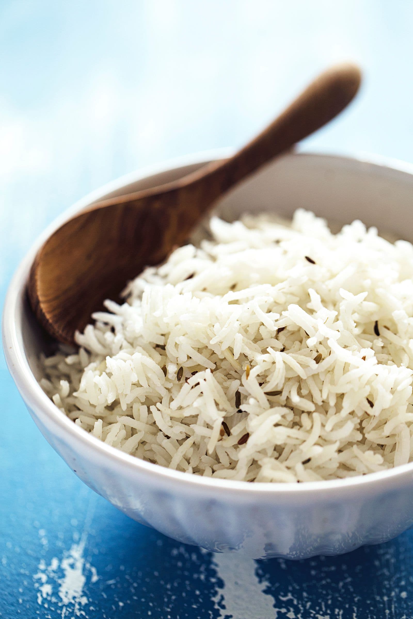 Arroz basmati fofo servido numa taça branca com colher de madeira.